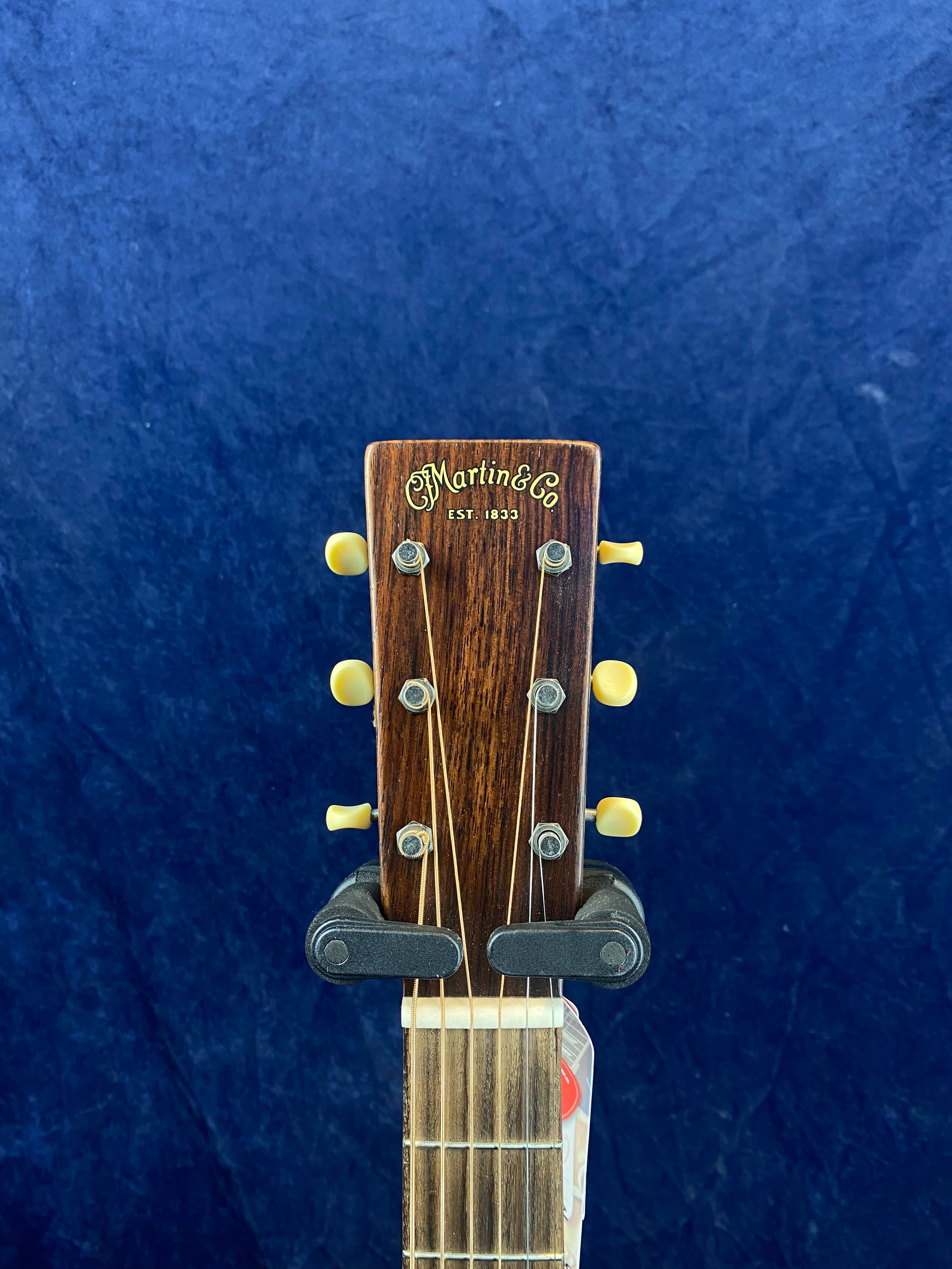 C. F. Martin & Co. acoustic guitar headstock with six yellow tuning pegs, metal tuner mounts, and "Est. 1833" in gold lettering on dark wood.