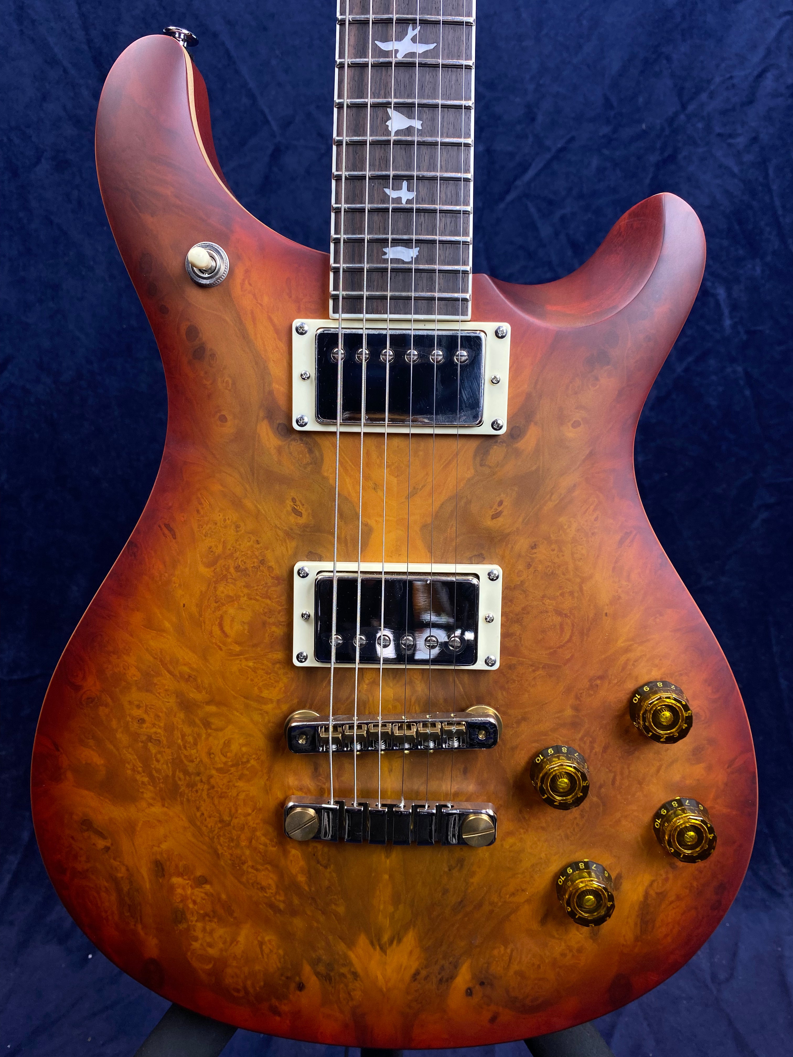 Electric guitar with a glossy, amber-burst wood finish, chrome hardware, two pickups, four amber knobs, and a fretboard inlaid with bird shapes.