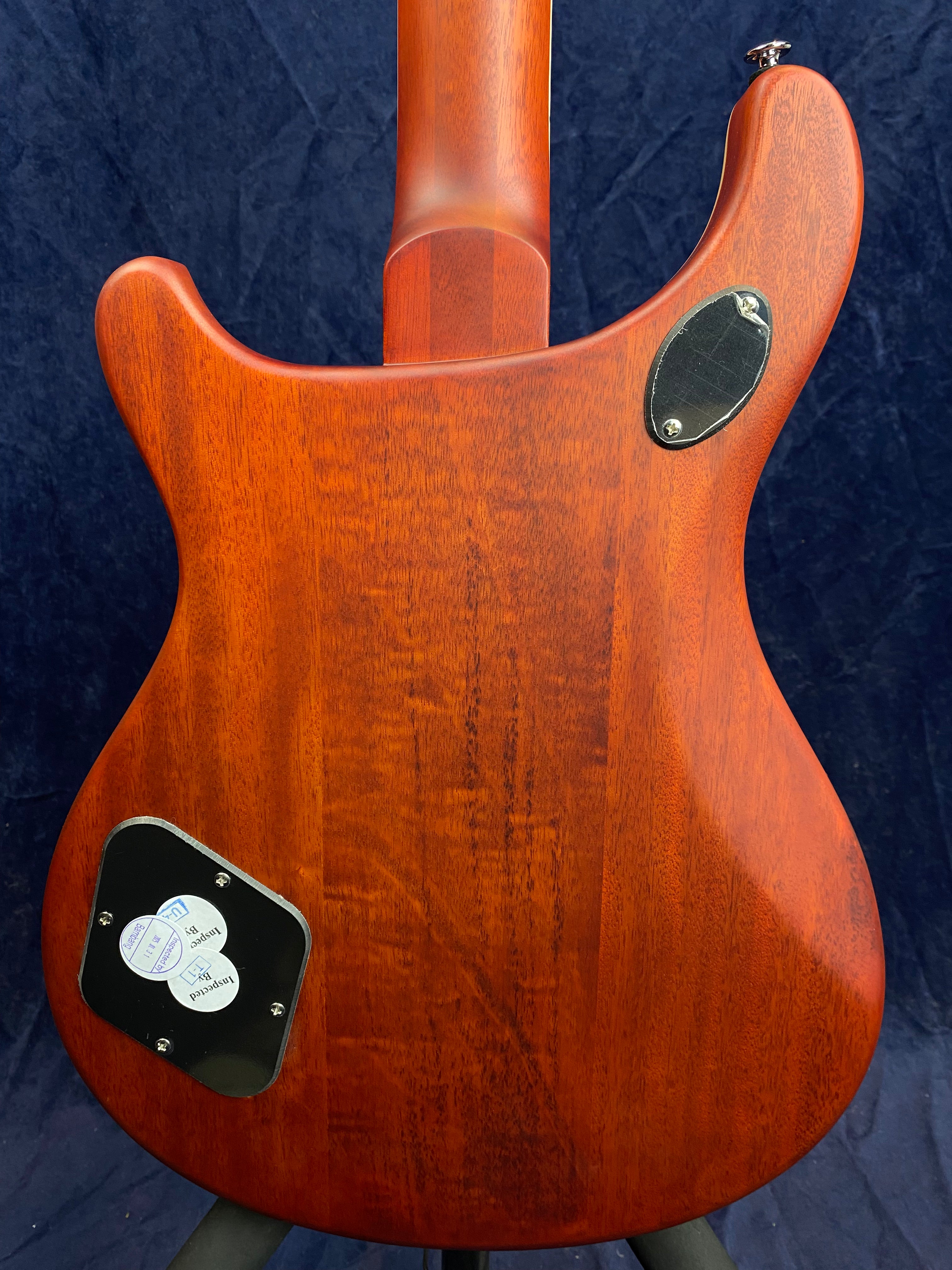 Rear view of an electric guitar with a reddish wood finish, two black access plates secured with screws, and a smooth, contoured body shape.