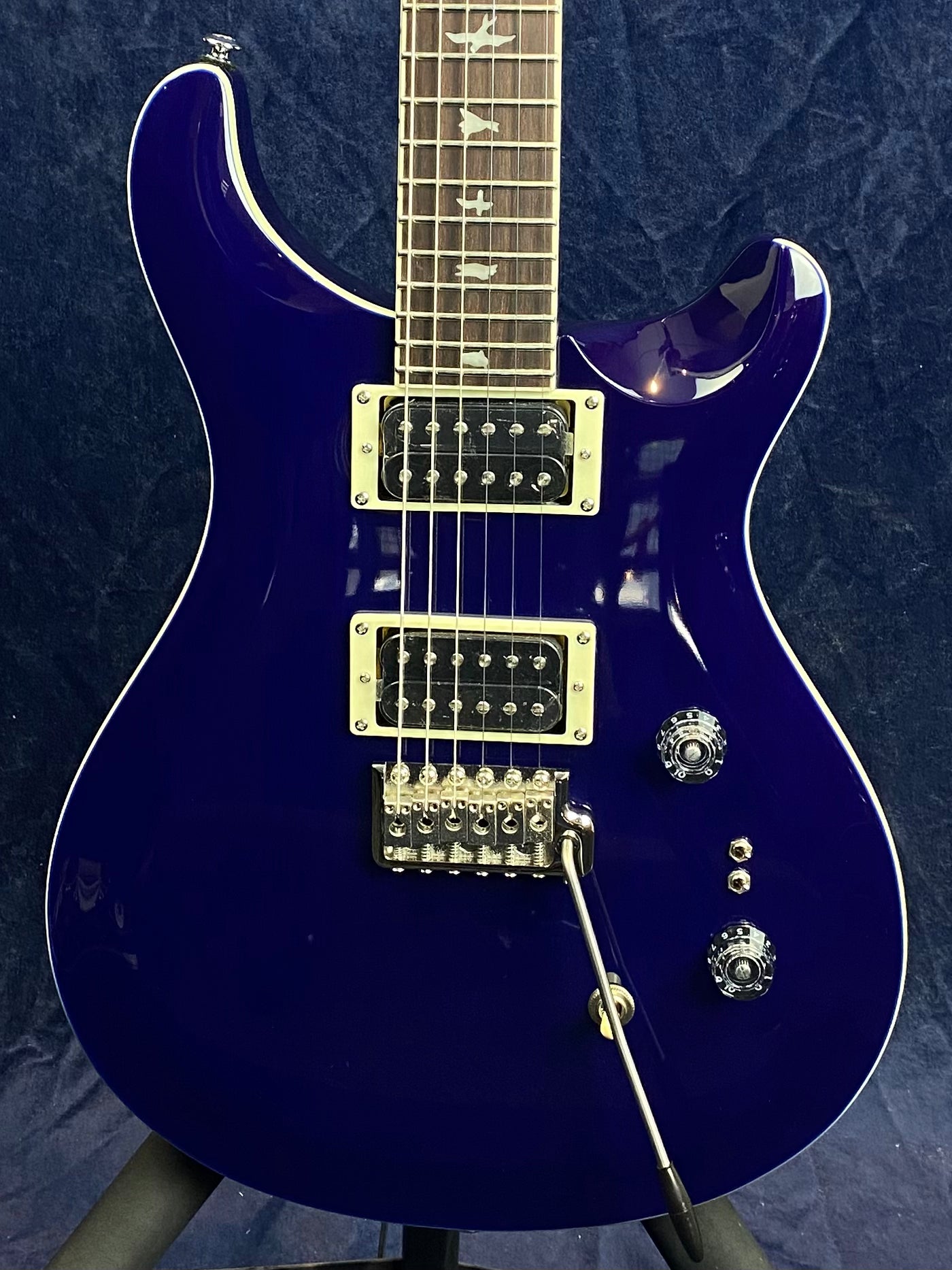 Deep blue electric guitar with two humbucker pickups, two control knobs, a tremolo bridge, and bird inlays on the rosewood fretboard.