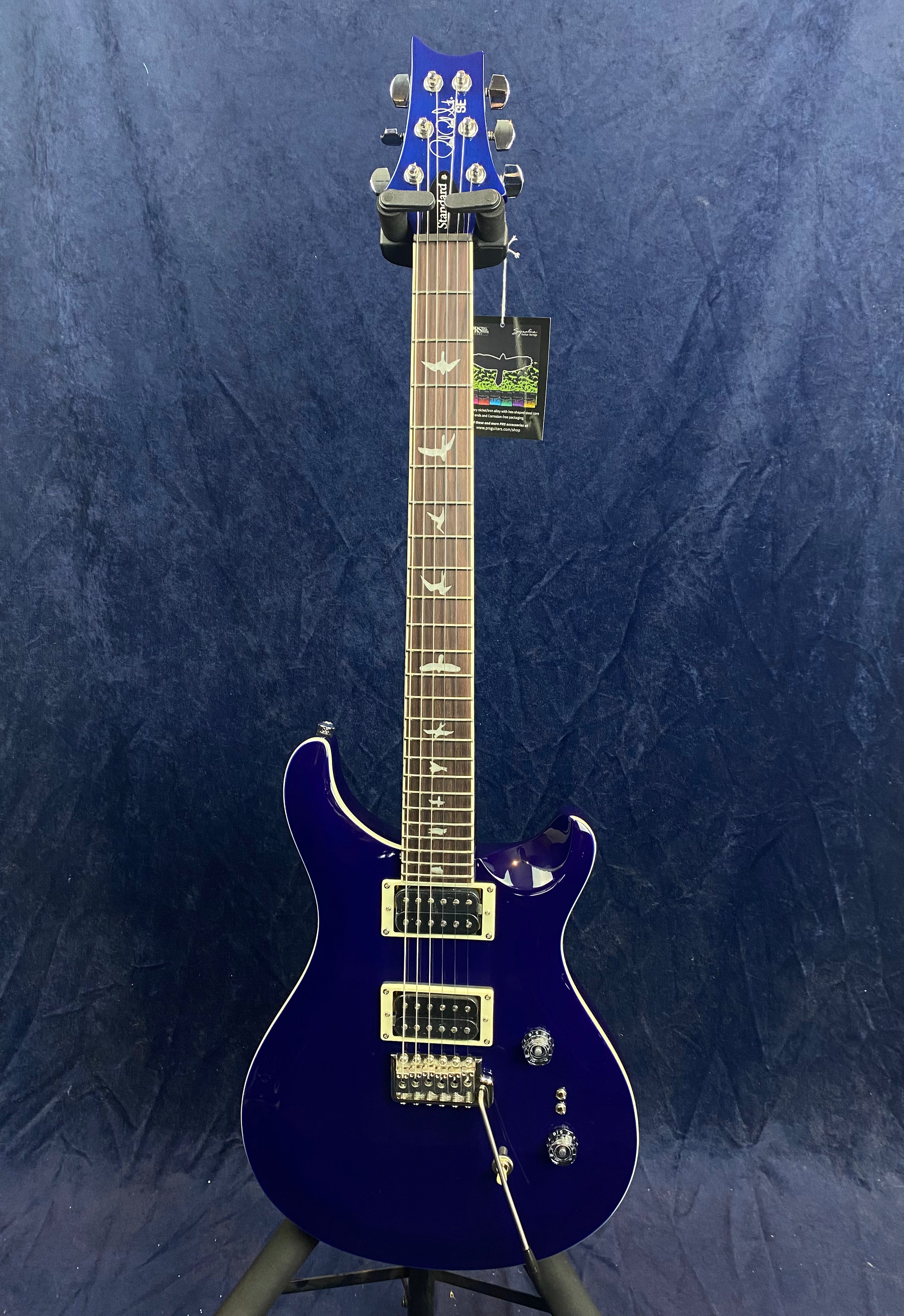 Blue electric guitar with bird inlays on the fretboard, two humbucker pickups, and three control knobs, displayed upright against a dark background.
