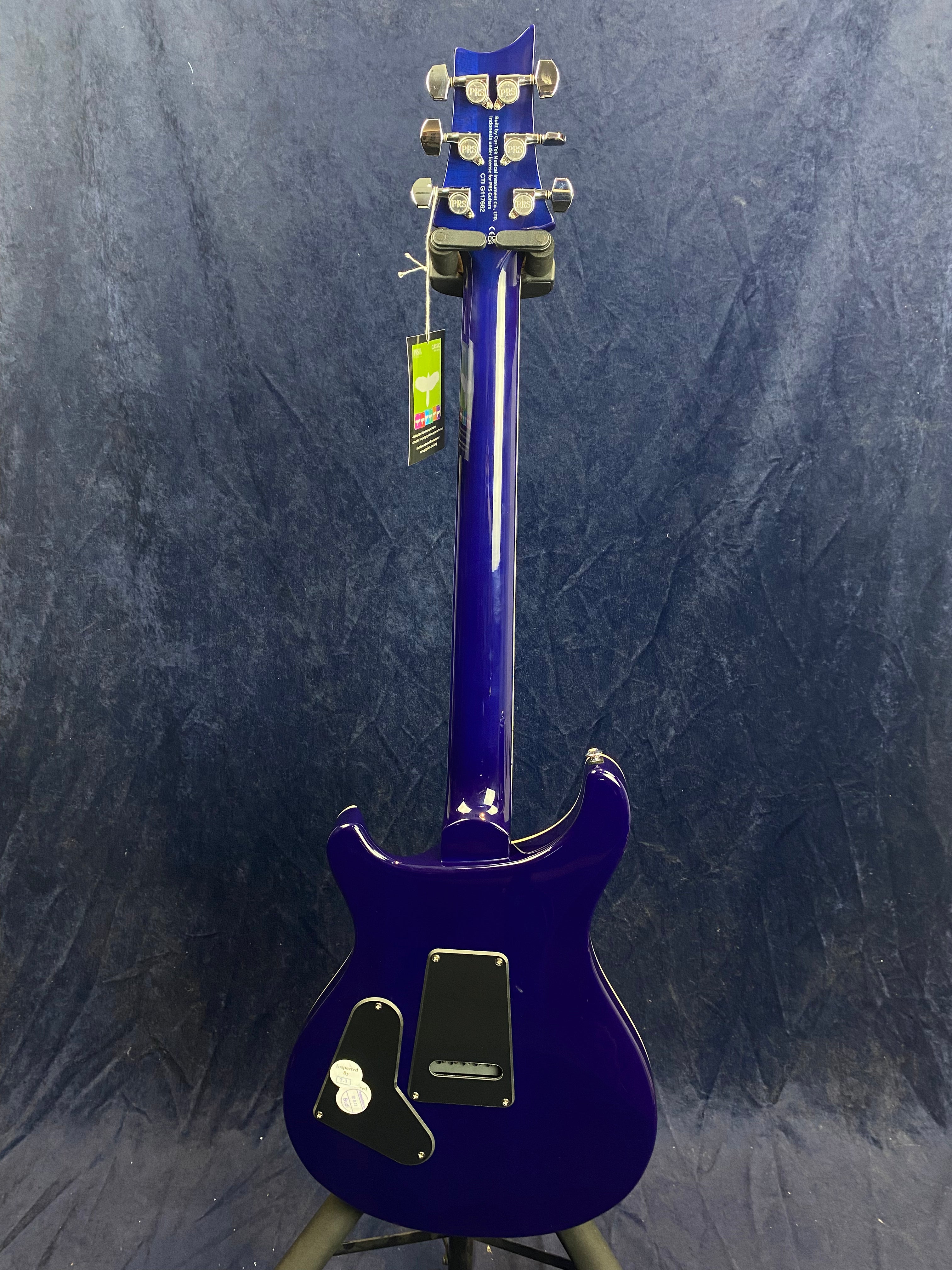 Bright purple electric guitar shown from the back; silver tuning pegs, two black backplates, and a hanging tag on the headstock.