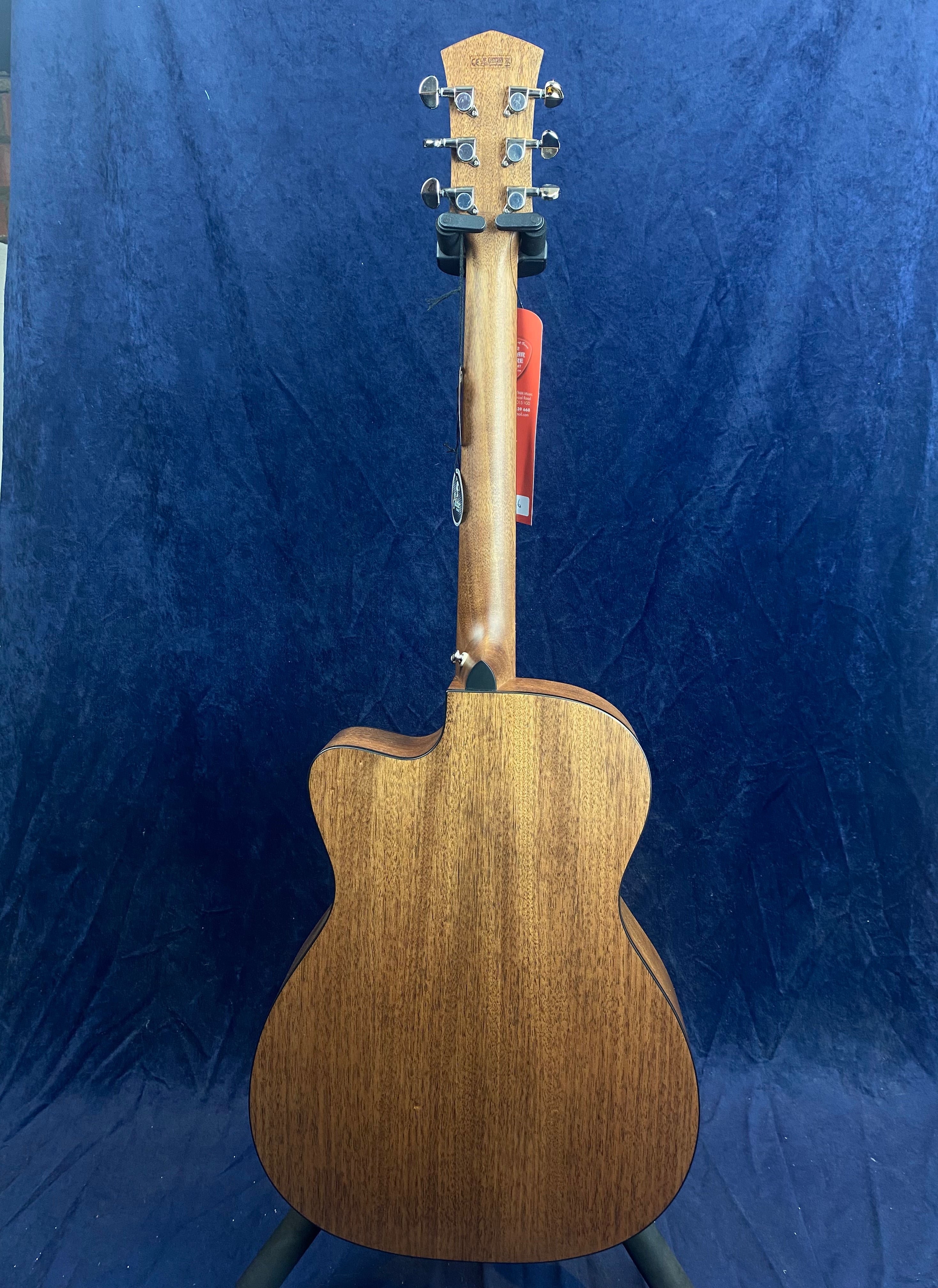 Back view of an acoustic guitar with a natural wood finish, six tuning pegs, and a cutaway body shape against a dark blue background.