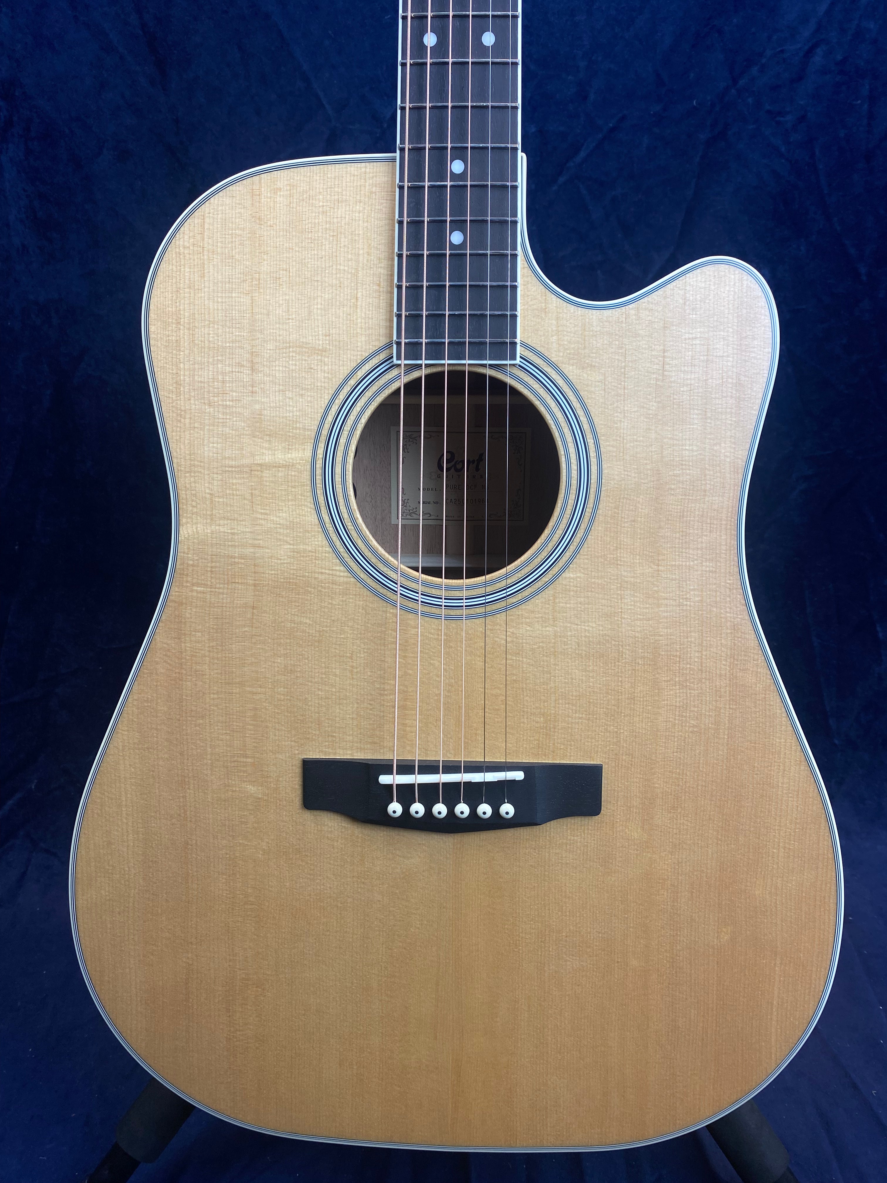 Natural wood-finish acoustic guitar with a cutaway body, round soundhole, black bridge, and six strings against a dark background.