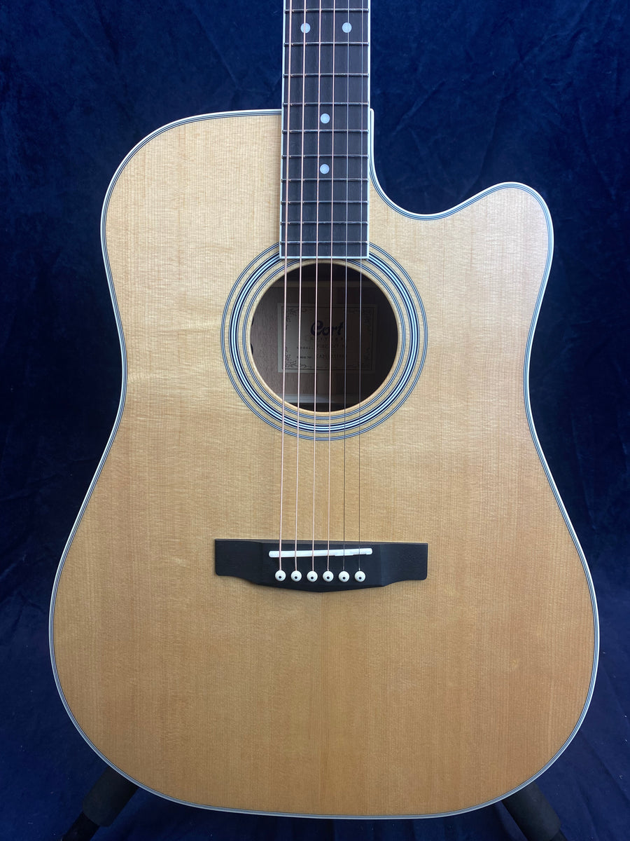 Natural wood-finish acoustic guitar with a cutaway body, round soundhole, black bridge, and six strings against a dark background.