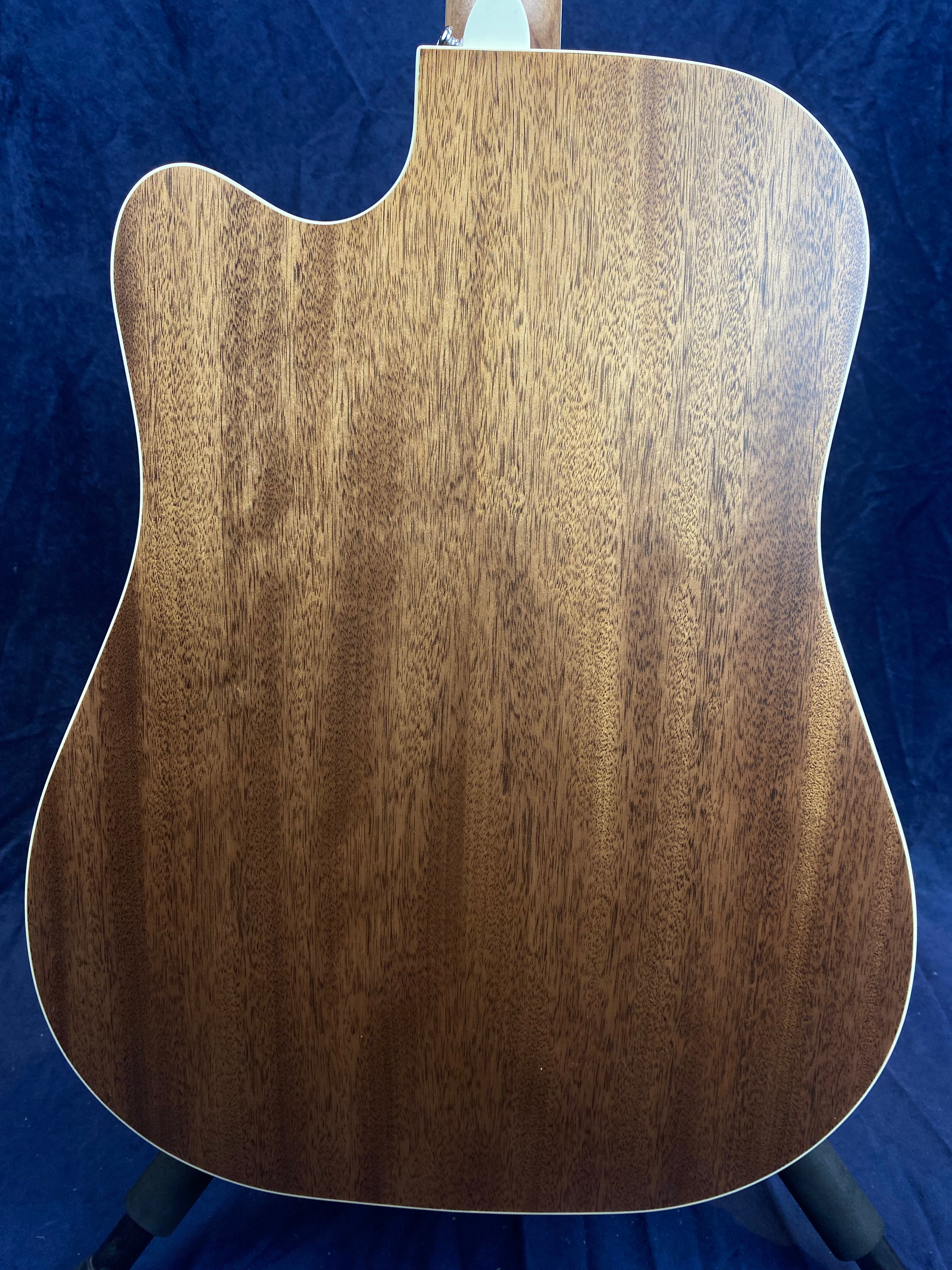 The back of an acoustic guitar made of light brown wood with visible grain patterns and a smooth, glossy finish.