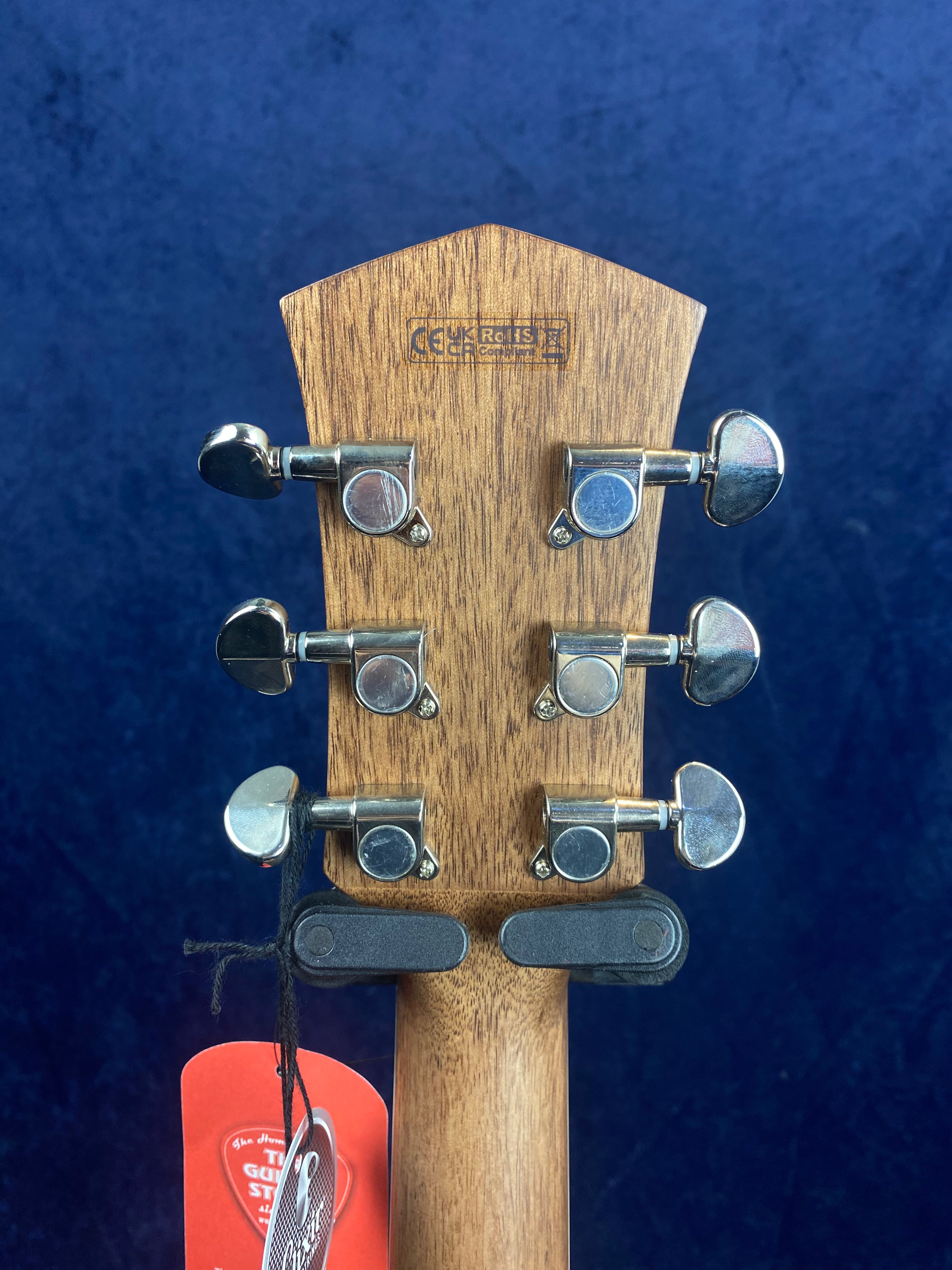 Six chrome tuning pegs are arranged in two rows on a wooden acoustic guitar headstock, with tags hanging from the left side.