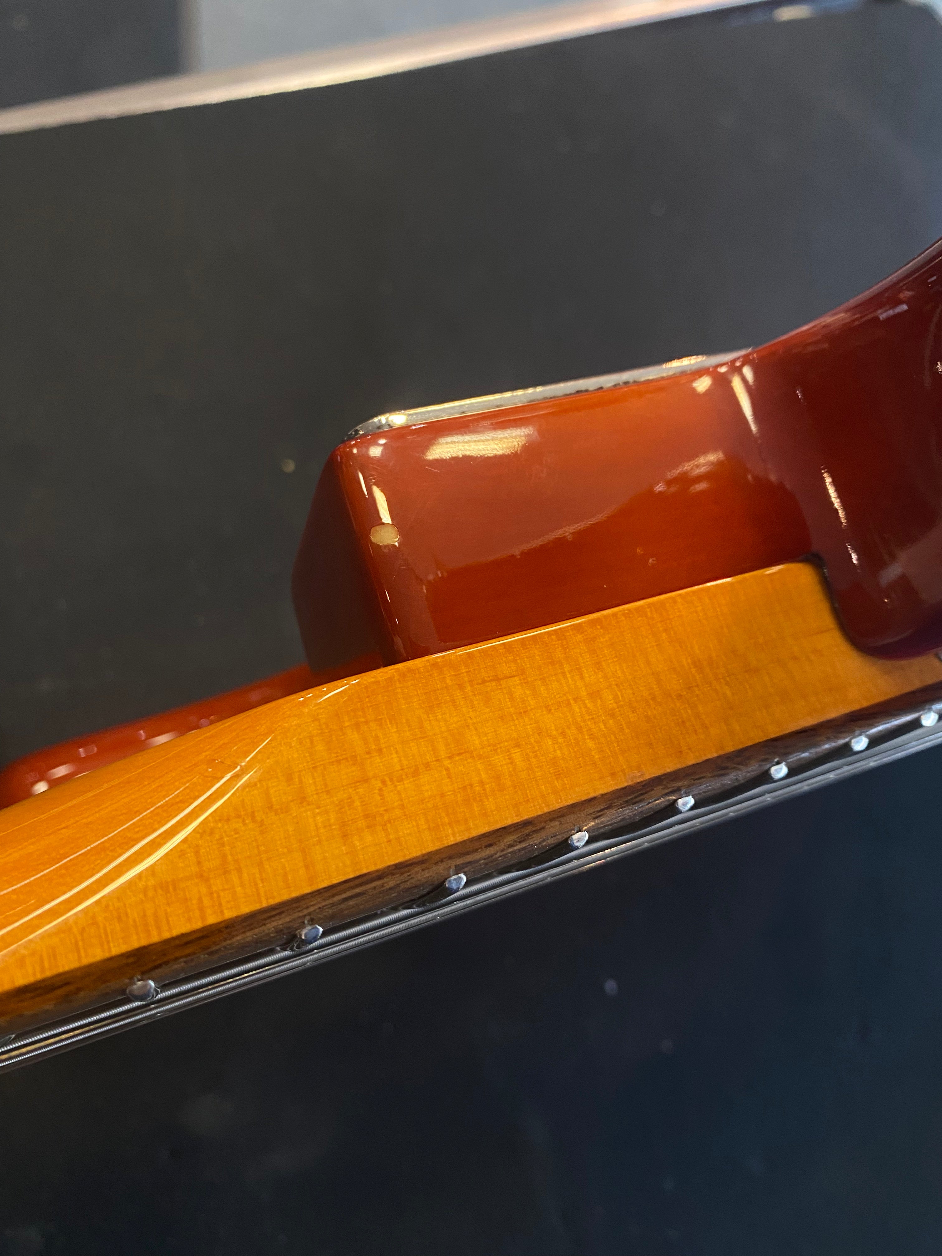 Close-up of an electric guitar neck joint with glossy brown finish and visible wood grain; metal frets and dot markers along the fingerboard edge.
