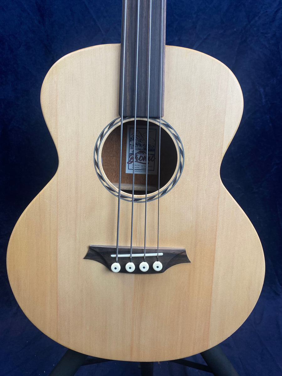 Acoustic bass guitar with a light wood body, four strings, a circular sound hole, and a dark wood bridge with white pins.