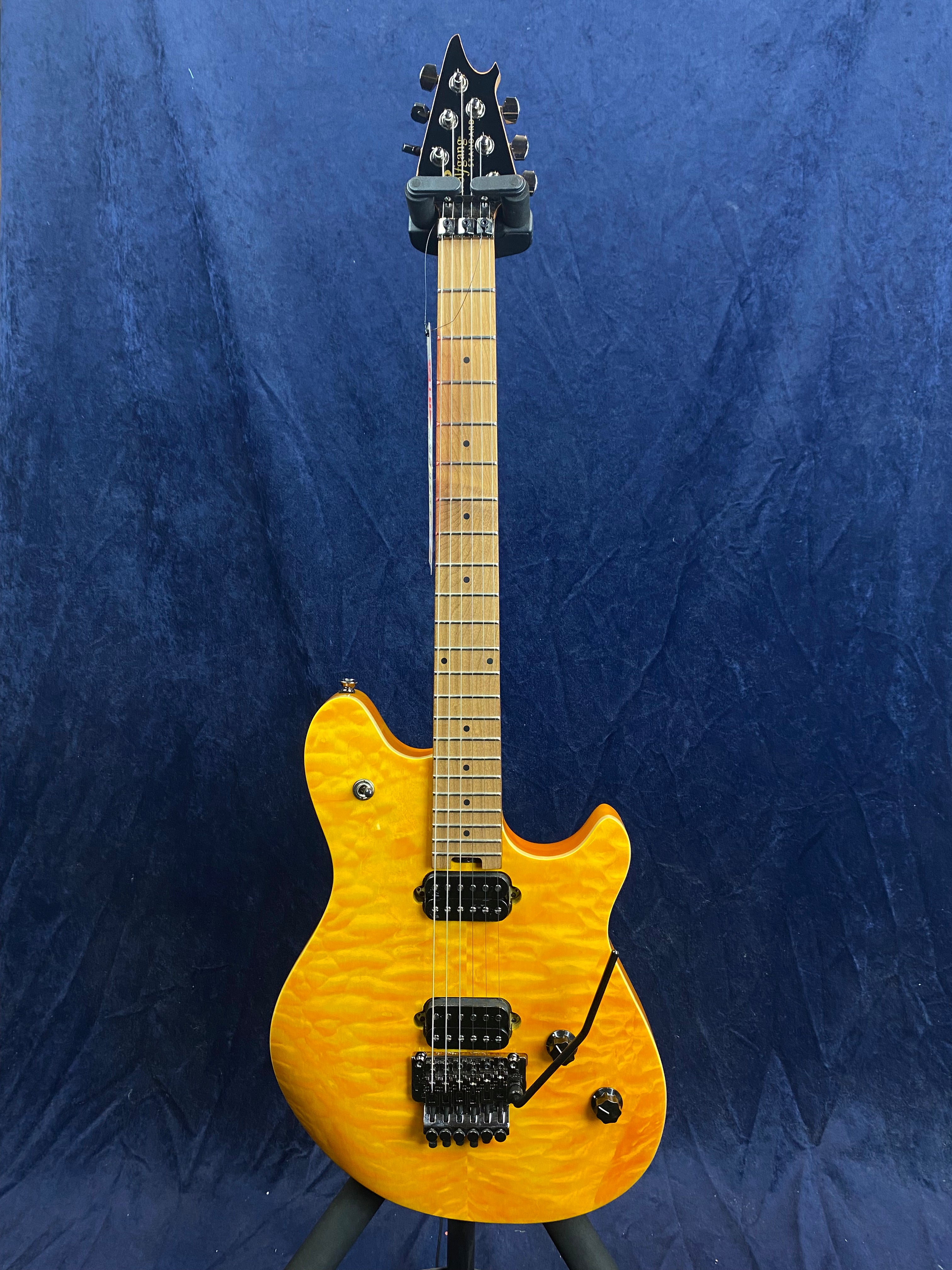 Electric guitar with a bright yellow quilted maple finish, two humbucker pickups, black hardware, and a whammy bar, displayed upright against a blue background.