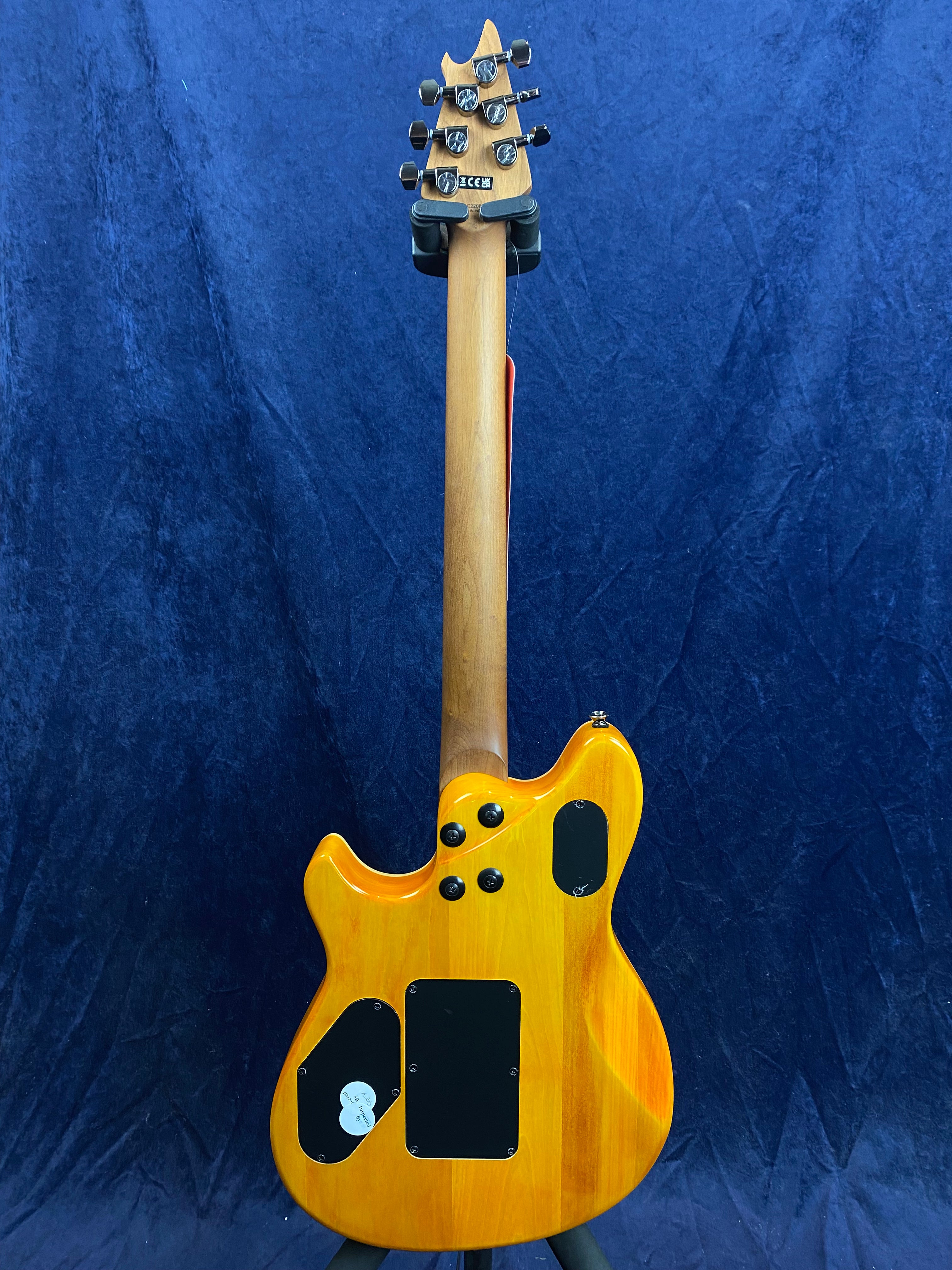 Electric guitar shown from the back, natural wood finish with three black access panels and four black knobs, set against a blue background.