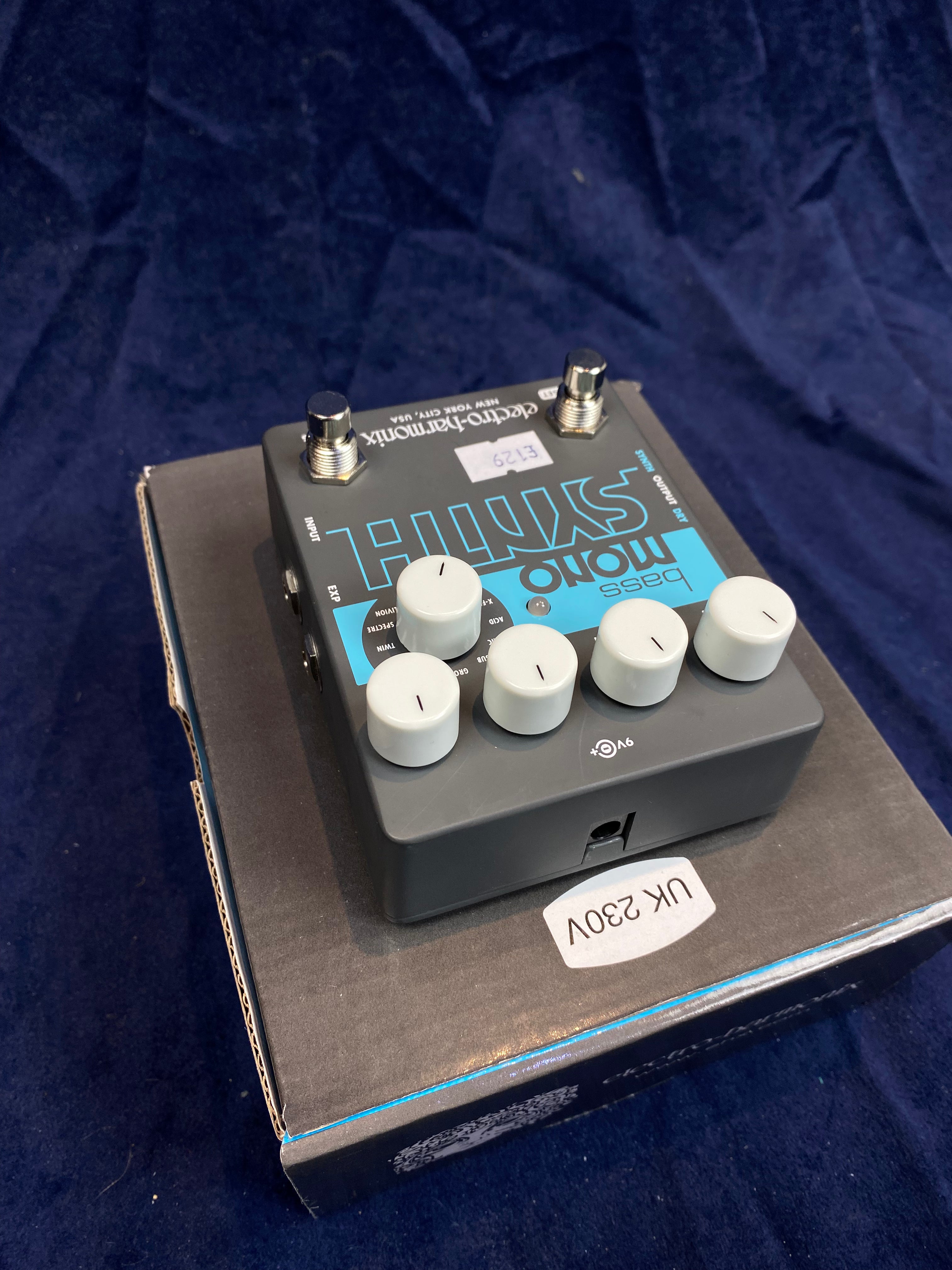 Electro-Harmonix Bass Mono Synth FX pedal with six white knobs on top, two footswitches, resting on its box labeled UK 230V.