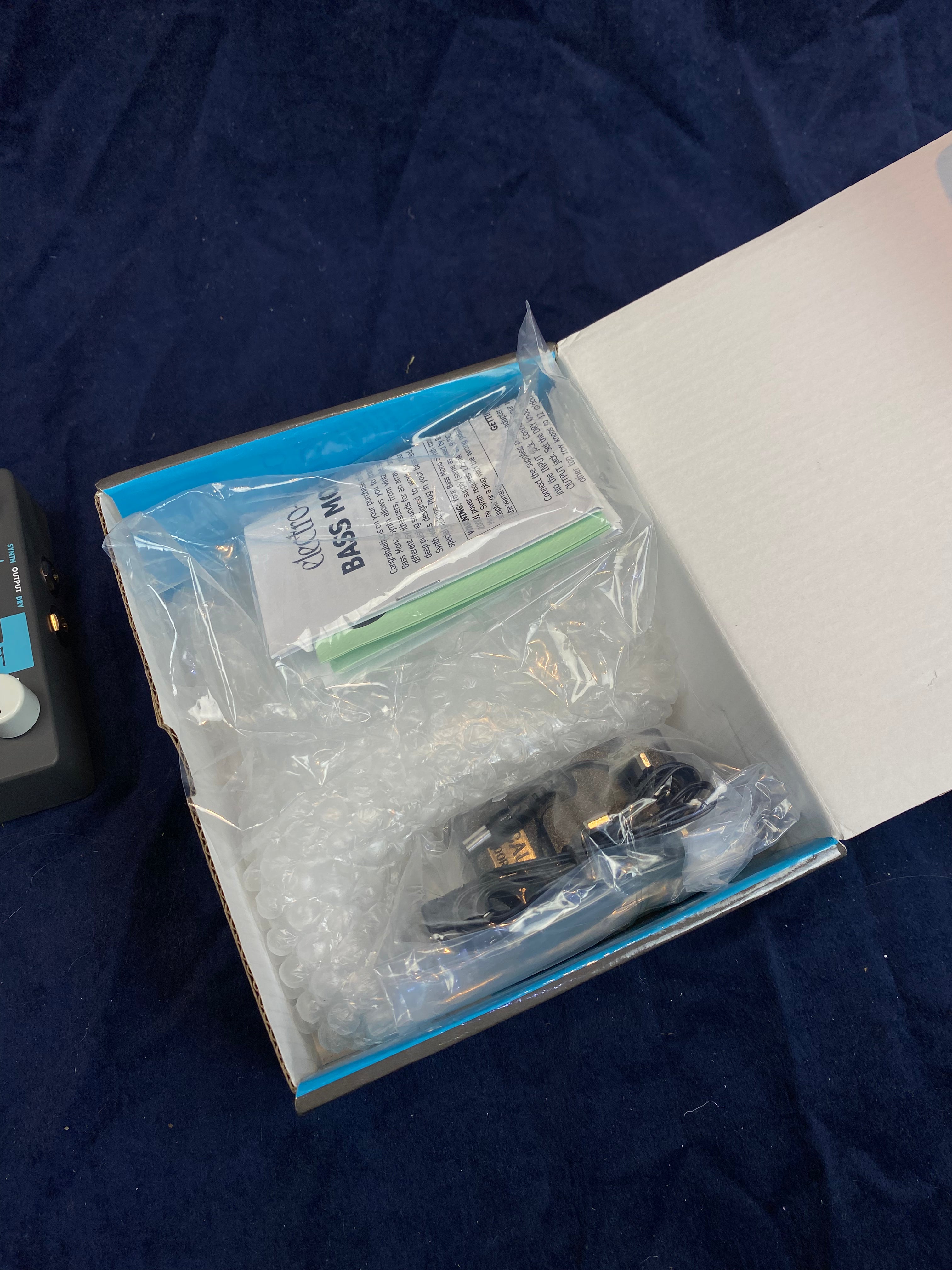 Open box for an FX pedal with bubble wrap, plug adaptor, cables, and a folded manual inside labeled "Bass Mini."