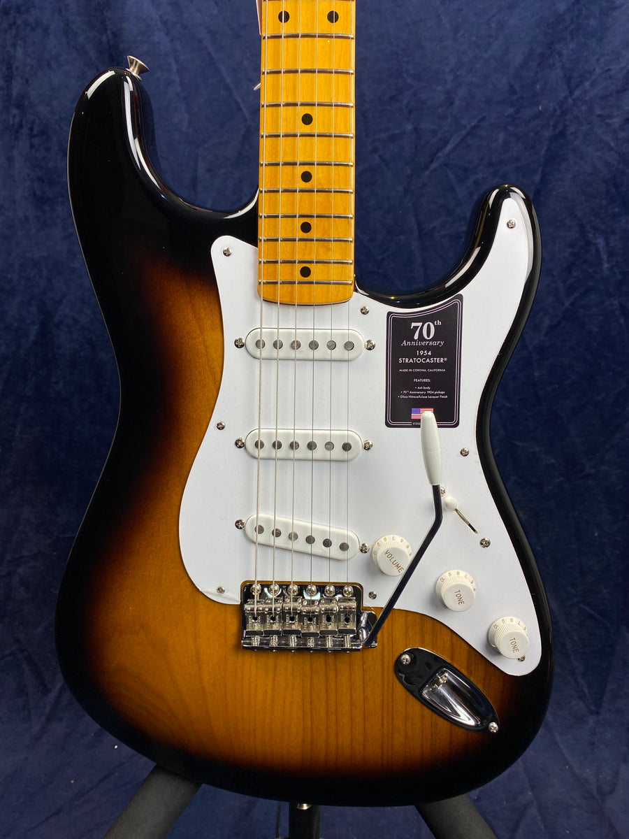 Sunburst electric guitar with a white pickguard, three single-coil pickups, control knobs, and a sticker marking the 70th Anniversary Stratocaster.