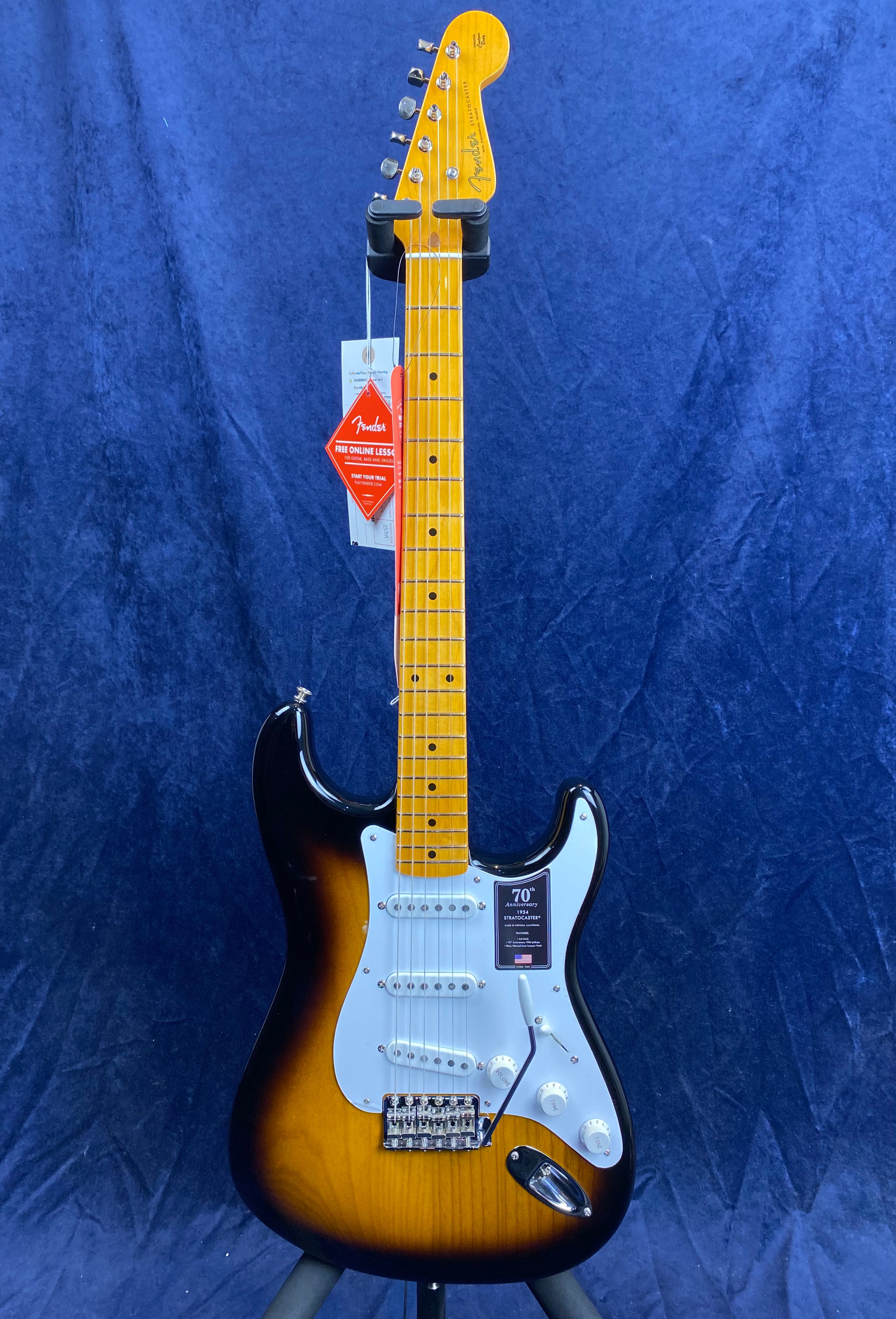 Fender electric guitar with a sunburst finish, white pickguard, maple neck, and product tags hanging from the headstock.