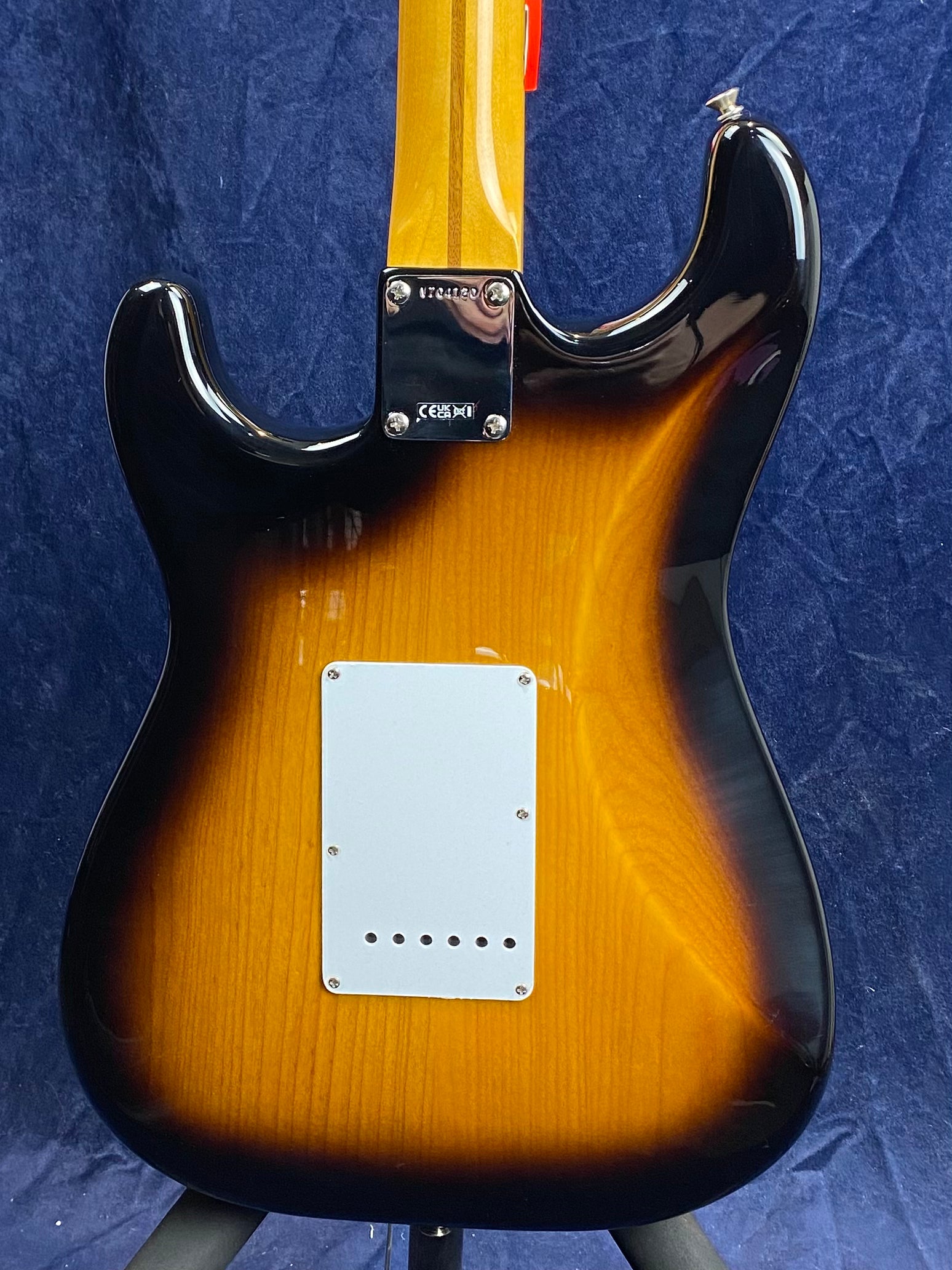 Sunburst electric guitar viewed from the back, showing wood grain, white rectangular backplate, and a glossy finish with black edges.