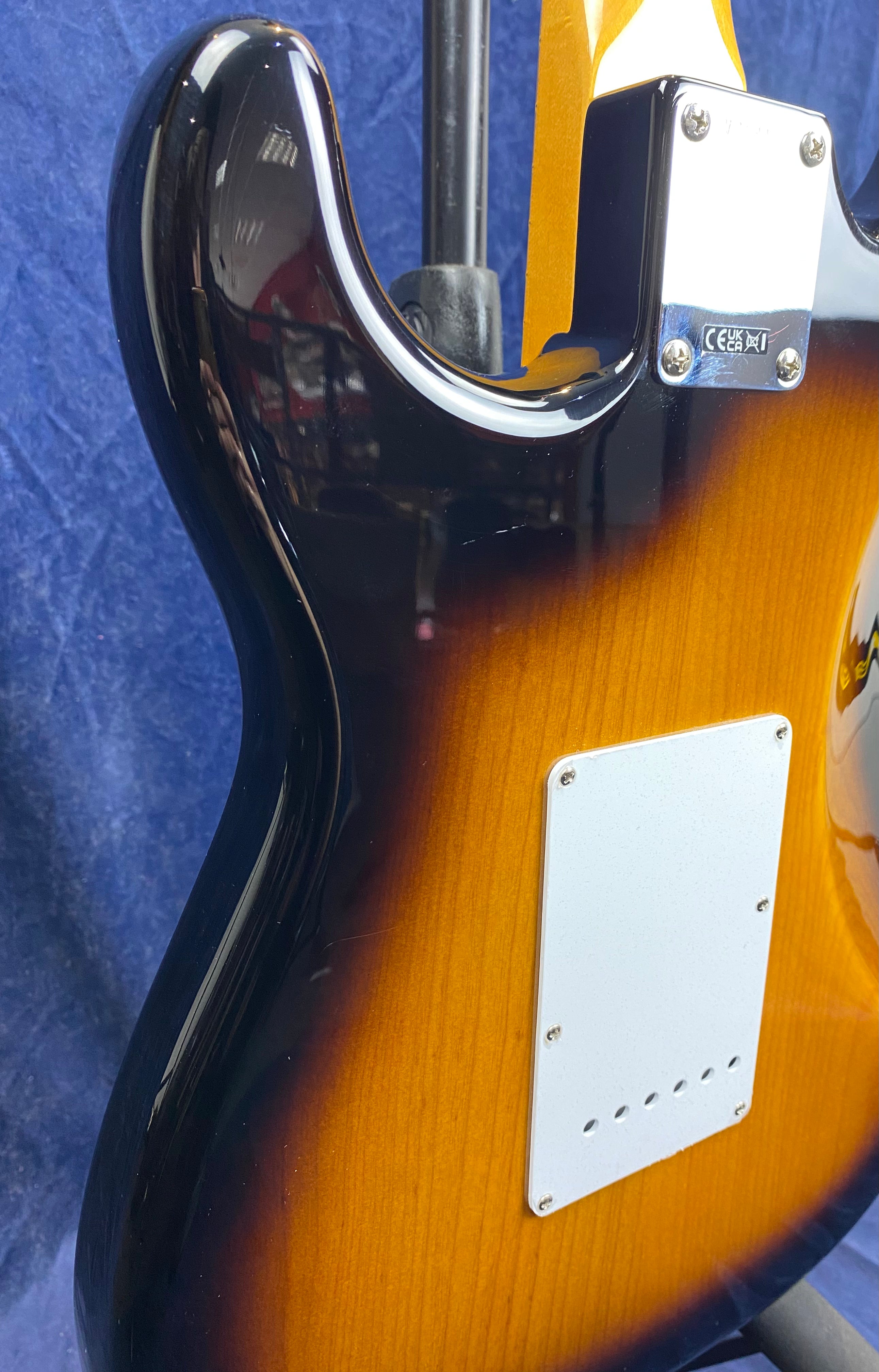 Sunburst electric guitar back with white back plate, four-bolt neck plate, and a glossy finish against a blue fabric background.