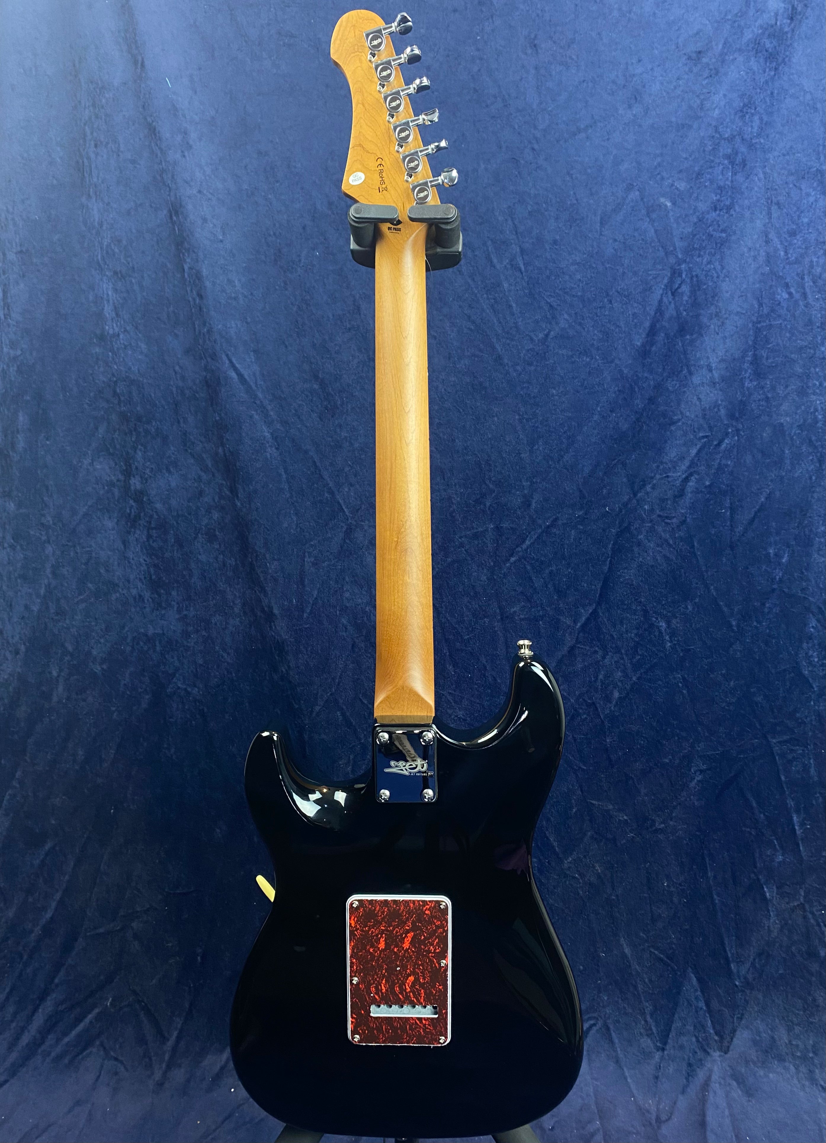 Black electric guitar shown from the back, natural wood neck, silver tuning pegs, and a red marbled back plate cover on the body.