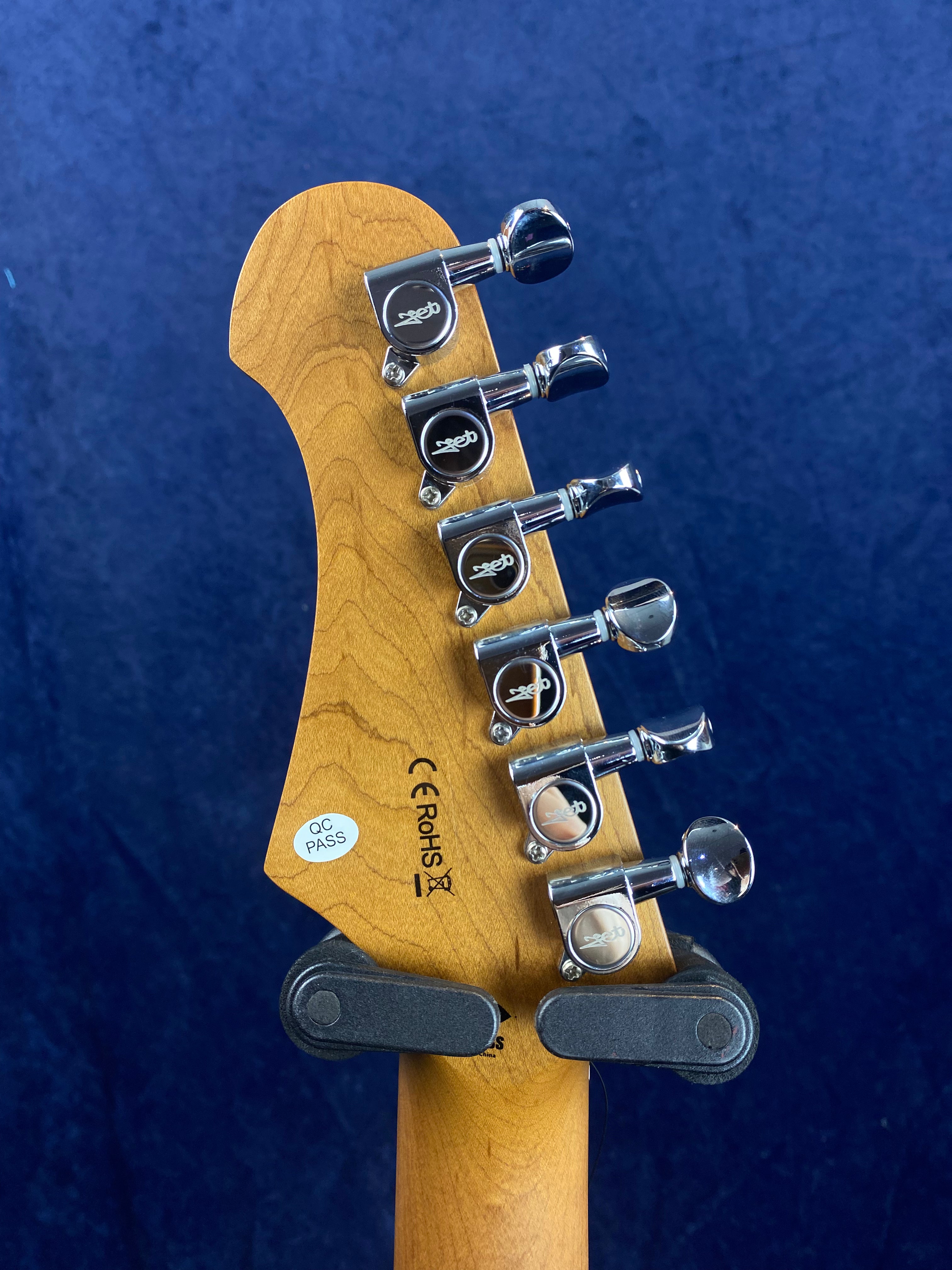 Six chrome tuning pegs on a natural wood electric guitar headstock, with certification markings and a QC pass sticker visible on the back.