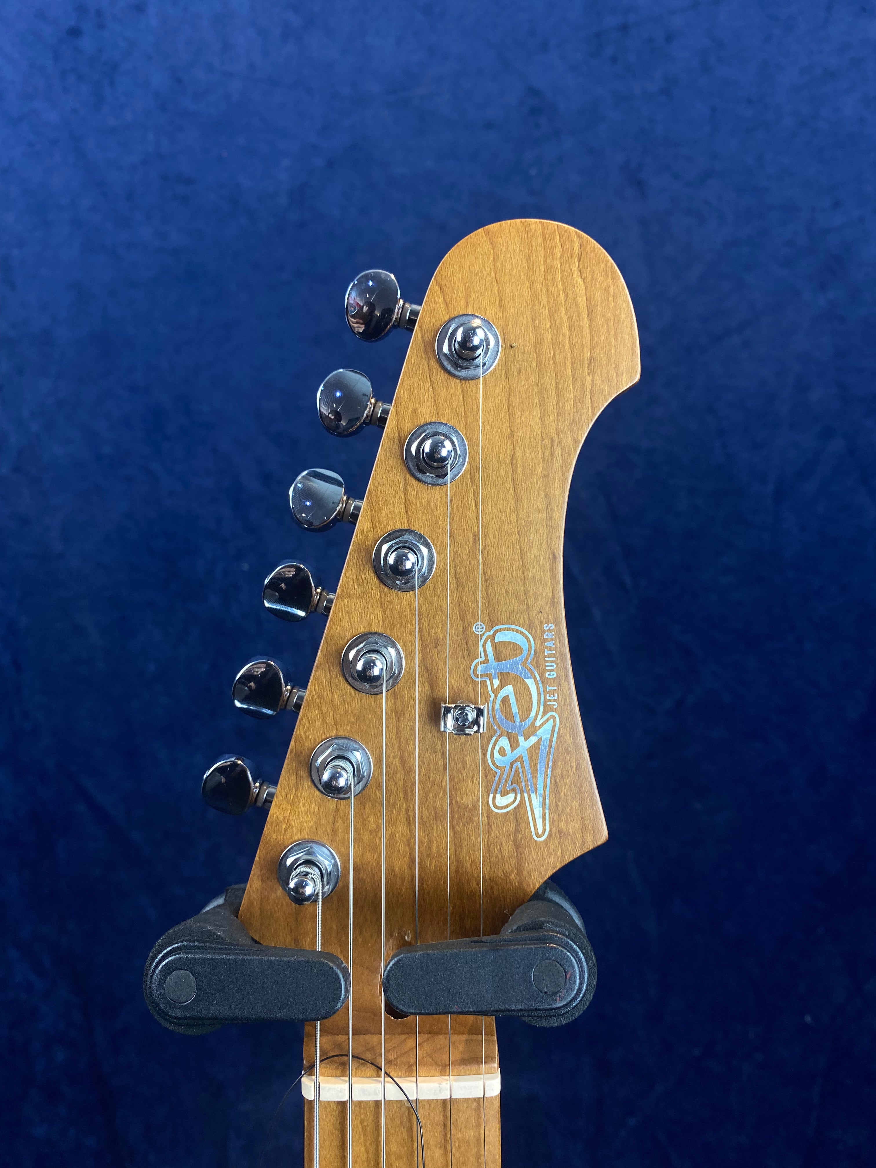 Light wooden electric guitar headstock with six chrome tuning pegs and "Jet Guitars" logo in white and blue script.