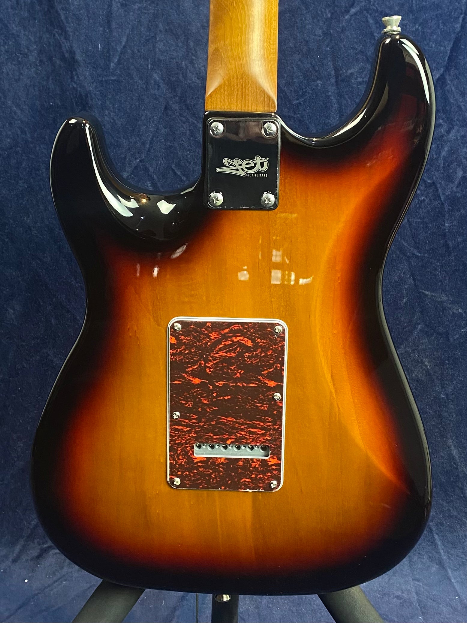 Sunburst-finish electric guitar back, tortoiseshell-patterned cavity cover, metal neck plate engraved with "Jet Guitars" logo.