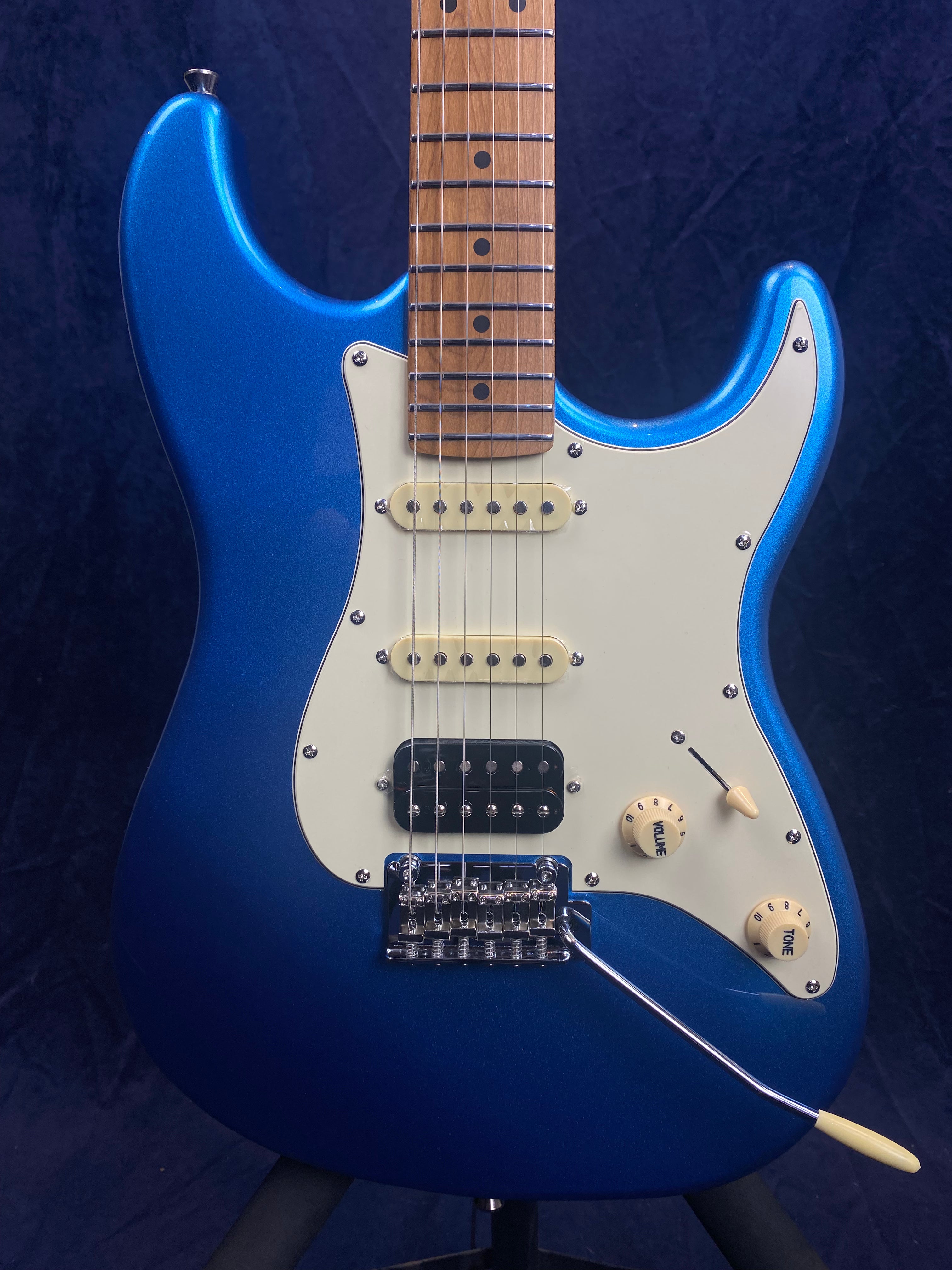 Blue electric guitar with white pickguard, two single-coil pickups, one black humbucker, three control knobs, and a tremolo bar.