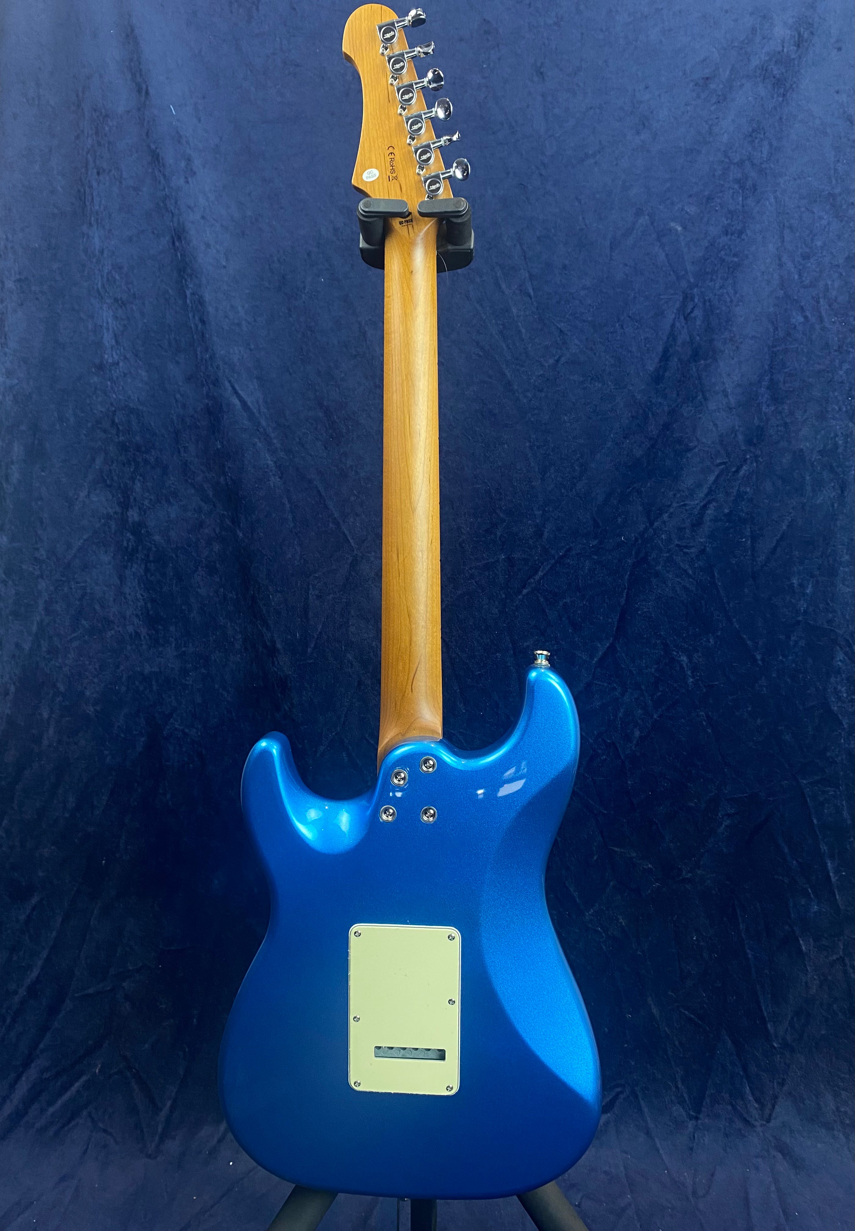 Electric guitar viewed from the back, metallic blue body, natural wood neck, silver tuners, and a white rectangular plate on the body.