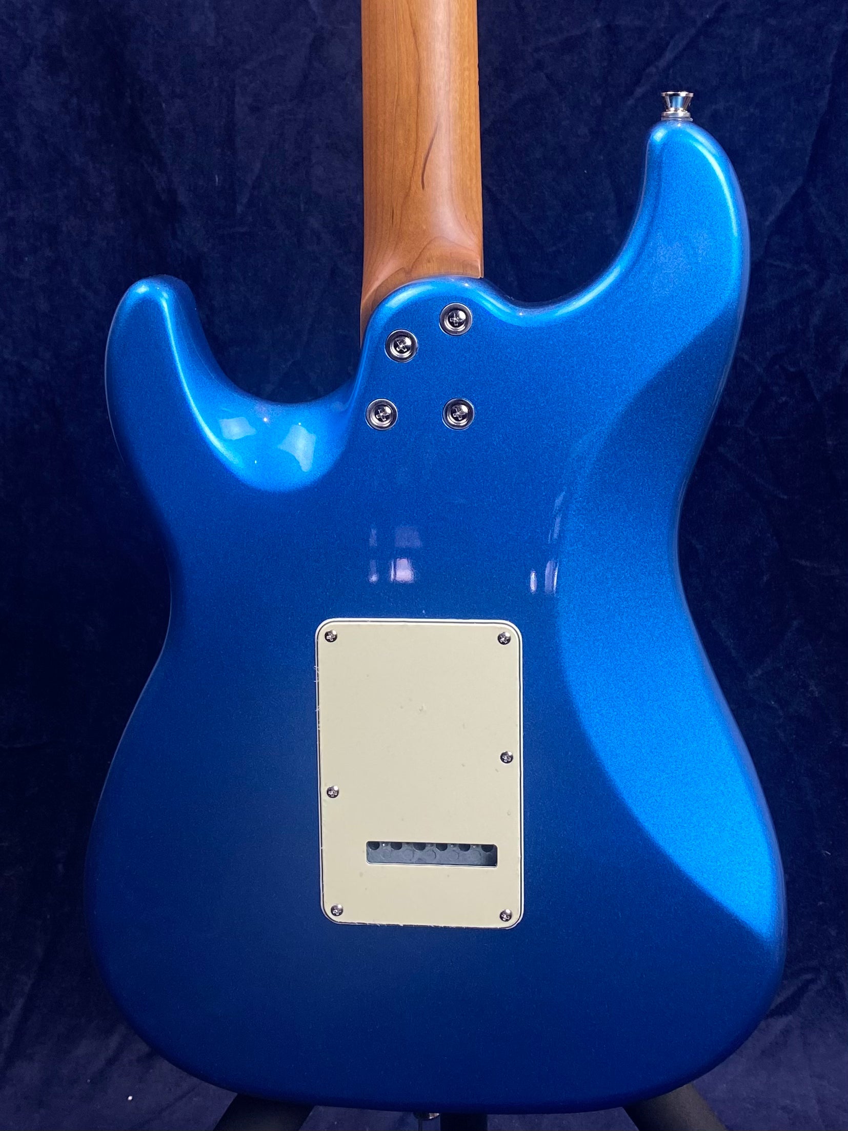 Back of an electric guitar with a glossy blue body, a natural wood neck, four neck bolts, and a rectangular cream cover plate near the bottom.