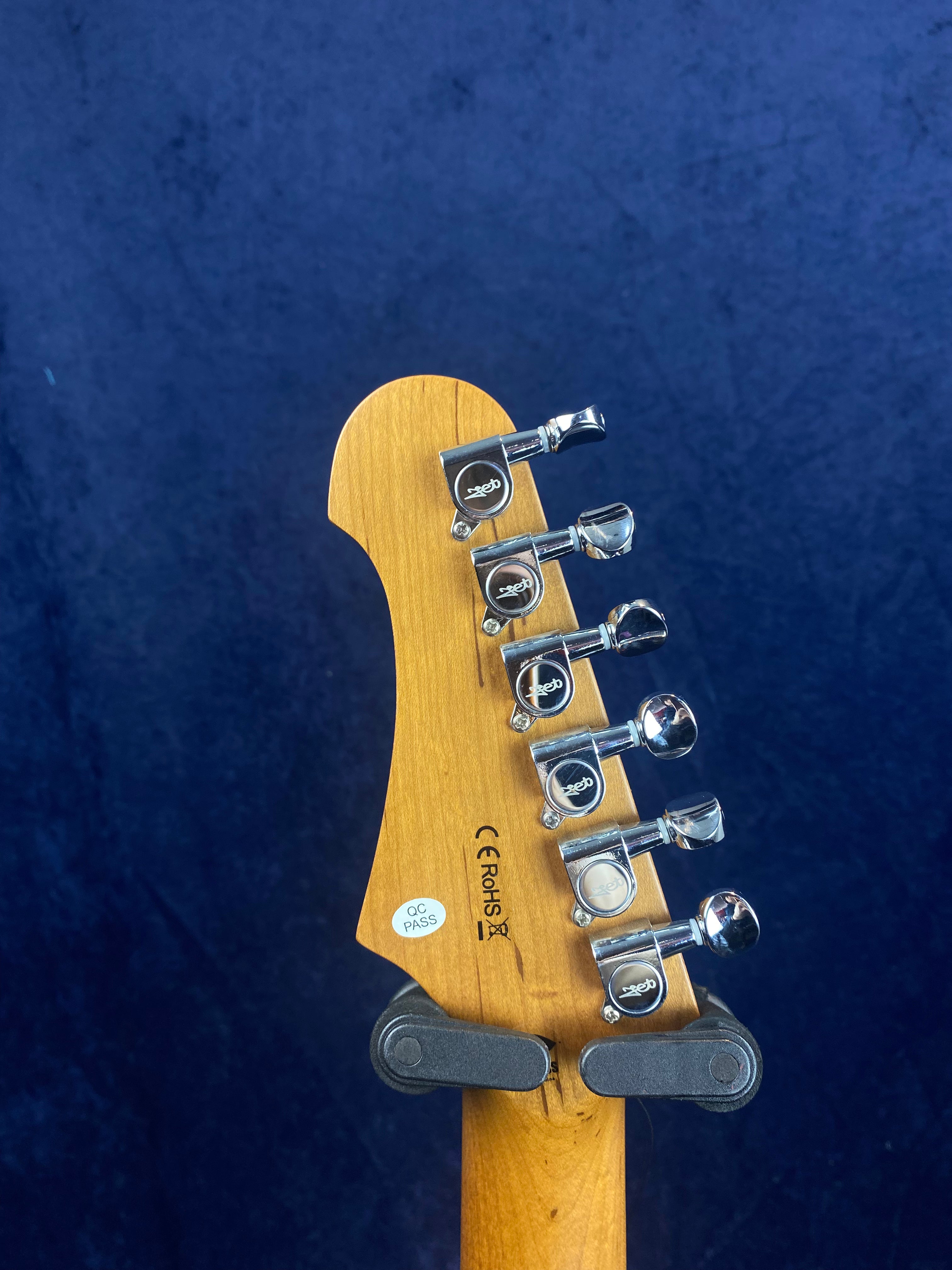 Six chrome tuning pegs on a light wood electric guitar headstock, with inspection and compliance stickers, set against a dark blue background.