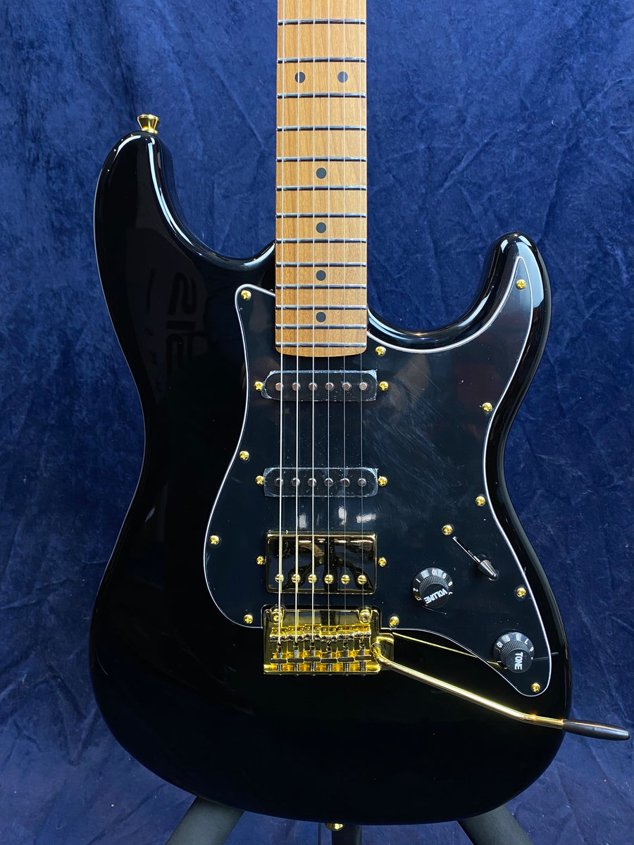 Black electric guitar with gold hardware, three pickups, two black control knobs, and a gold tremolo arm against a dark blue background.