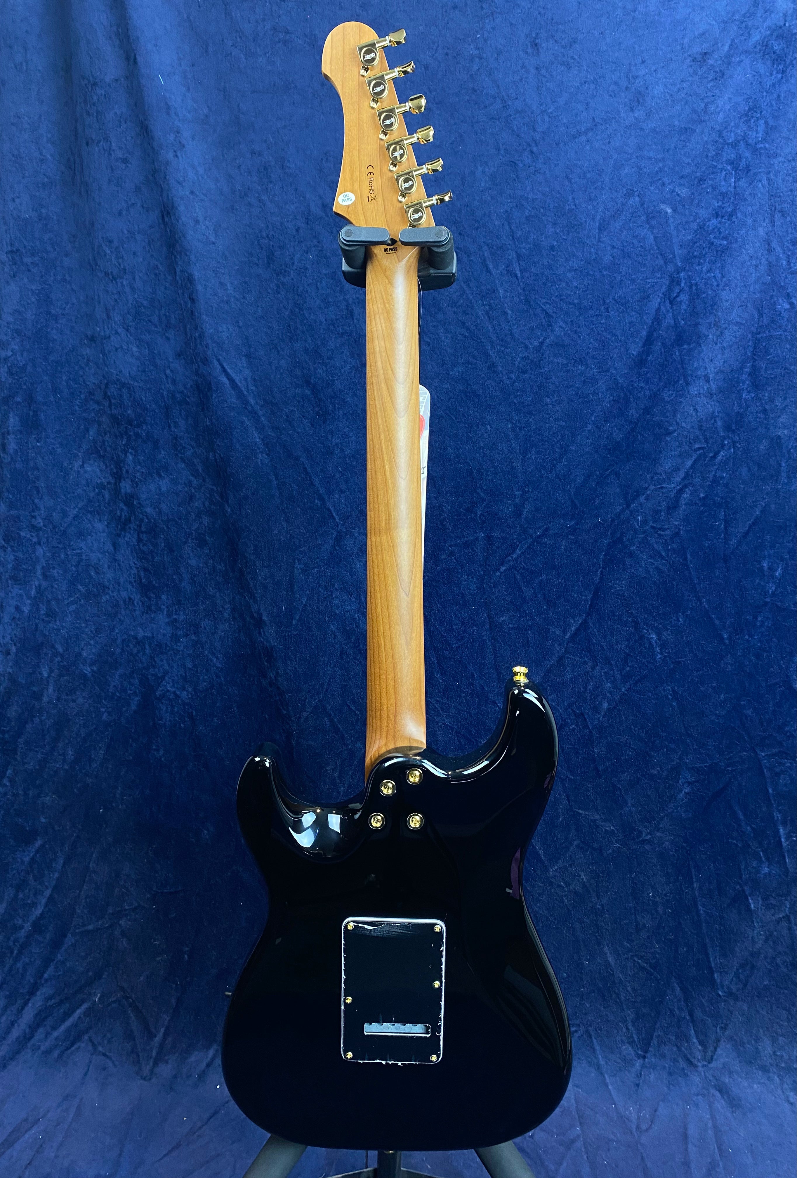 Glossy black electric guitar viewed from the back, showing a natural wood neck, six gold tuners, and a rectangular backplate on the body.