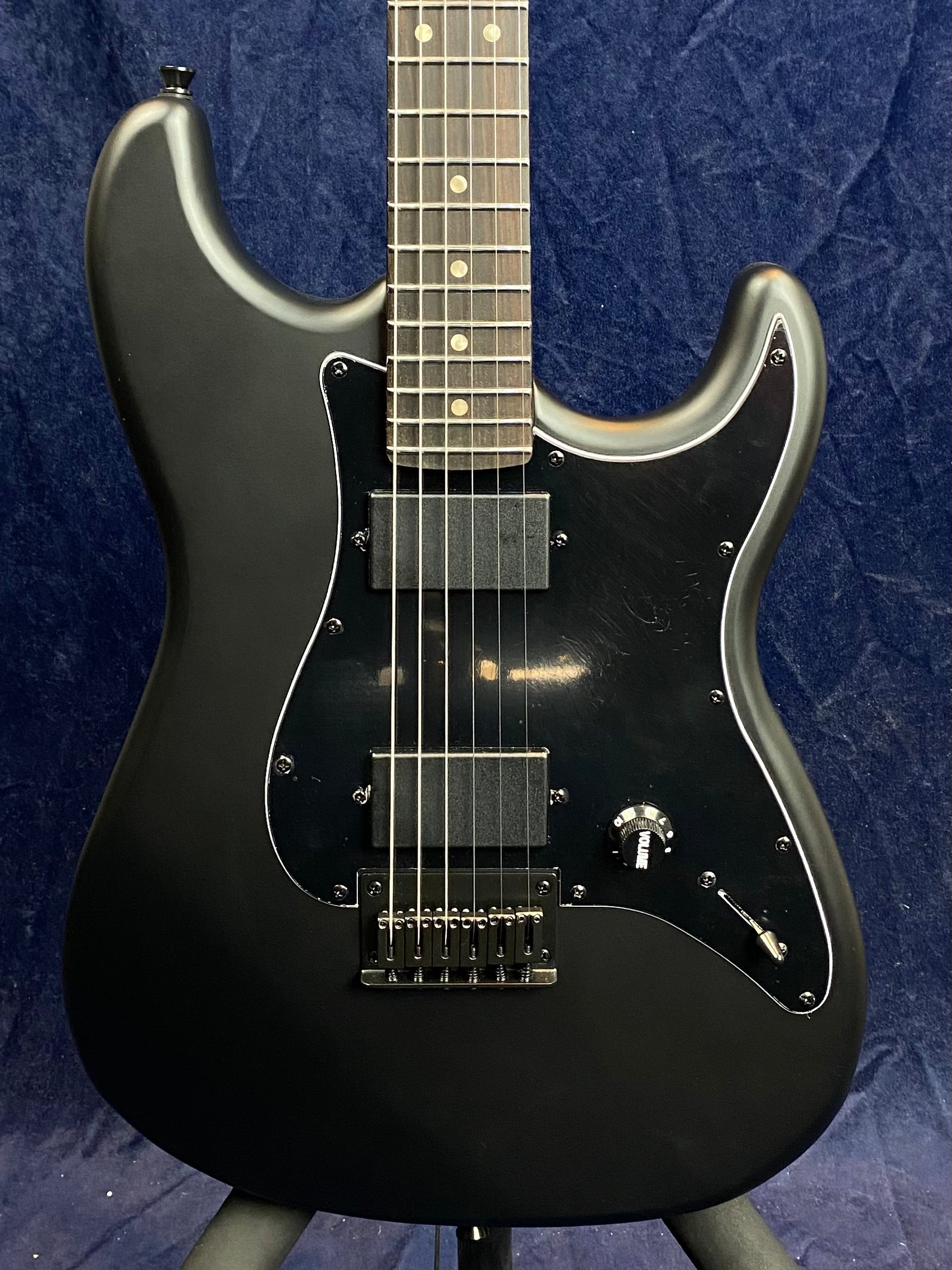 Black electric guitar with a matte finish, black pickguard, two rectangular pickups, single knob labeled "volume," and a toggle switch.