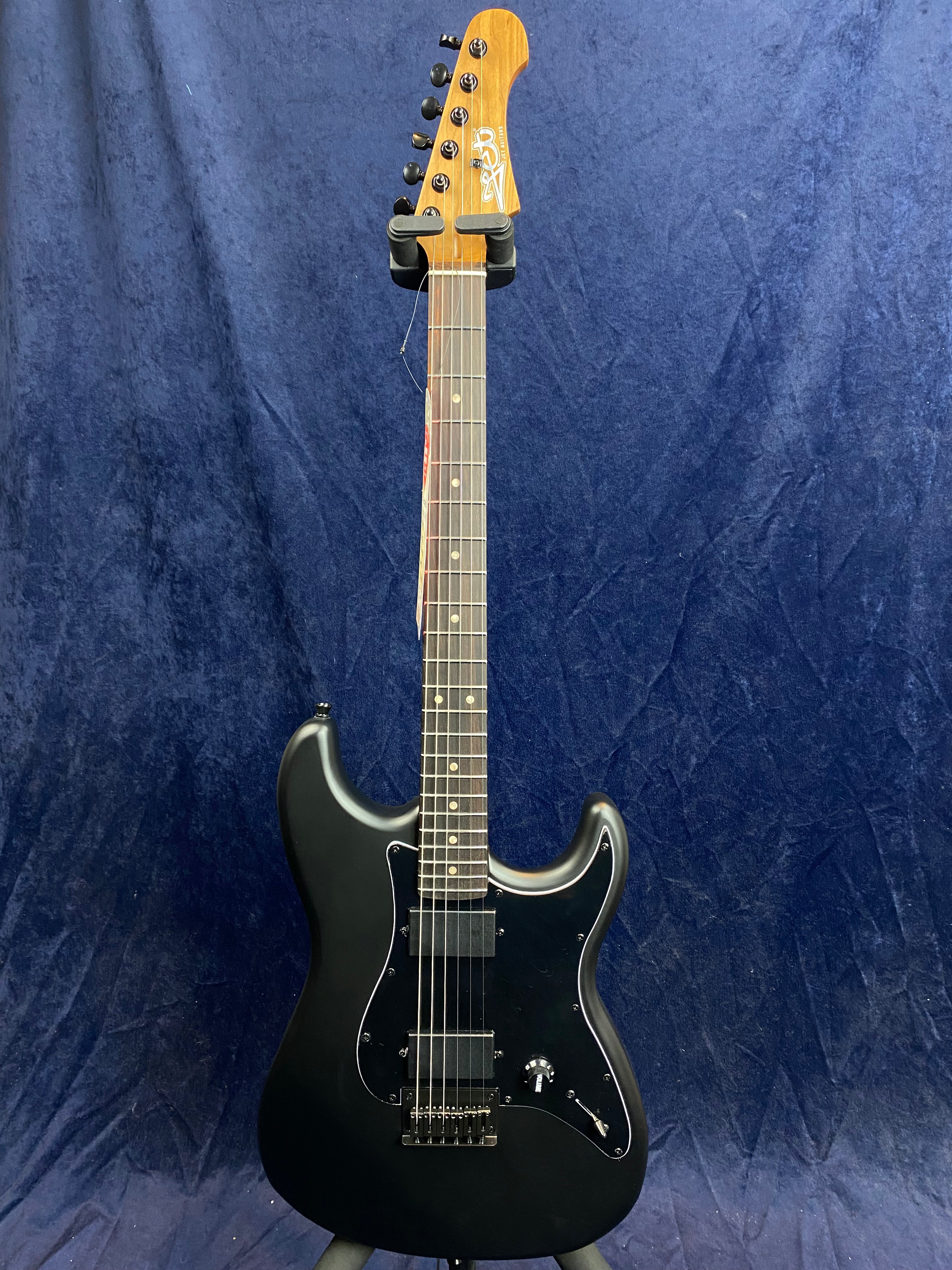 Matte black electric guitar with two humbucker pickups, a single volume knob, and a bolt-on maple neck, set against a dark blue background.