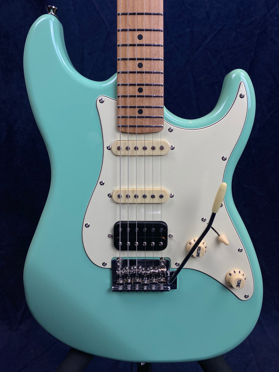 Guitare électrique turquoise avec pickguard blanc, trois micros, deux boutons de réglage crème et un vibrato métallique chromé.