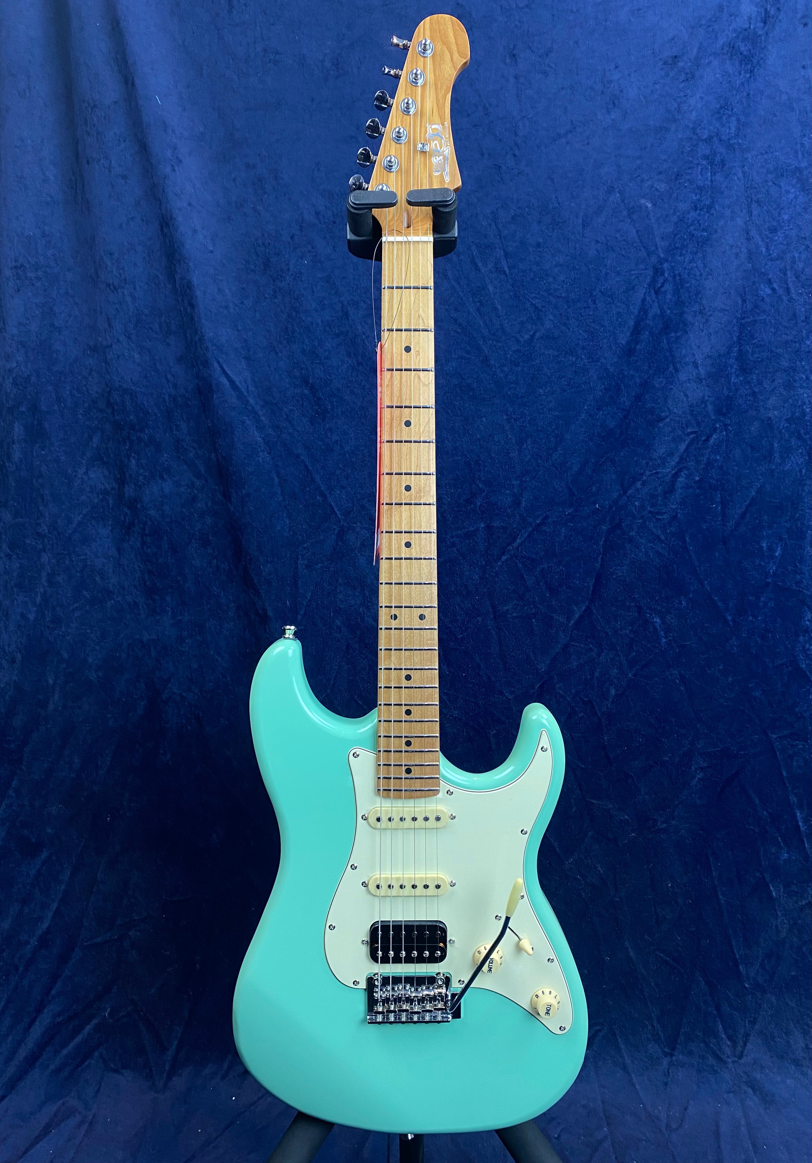 Guitare électrique turquoise à manche érable, trois micros, plaque blanche, six boutons argentés en tête, vibrato, fond bleu uni.