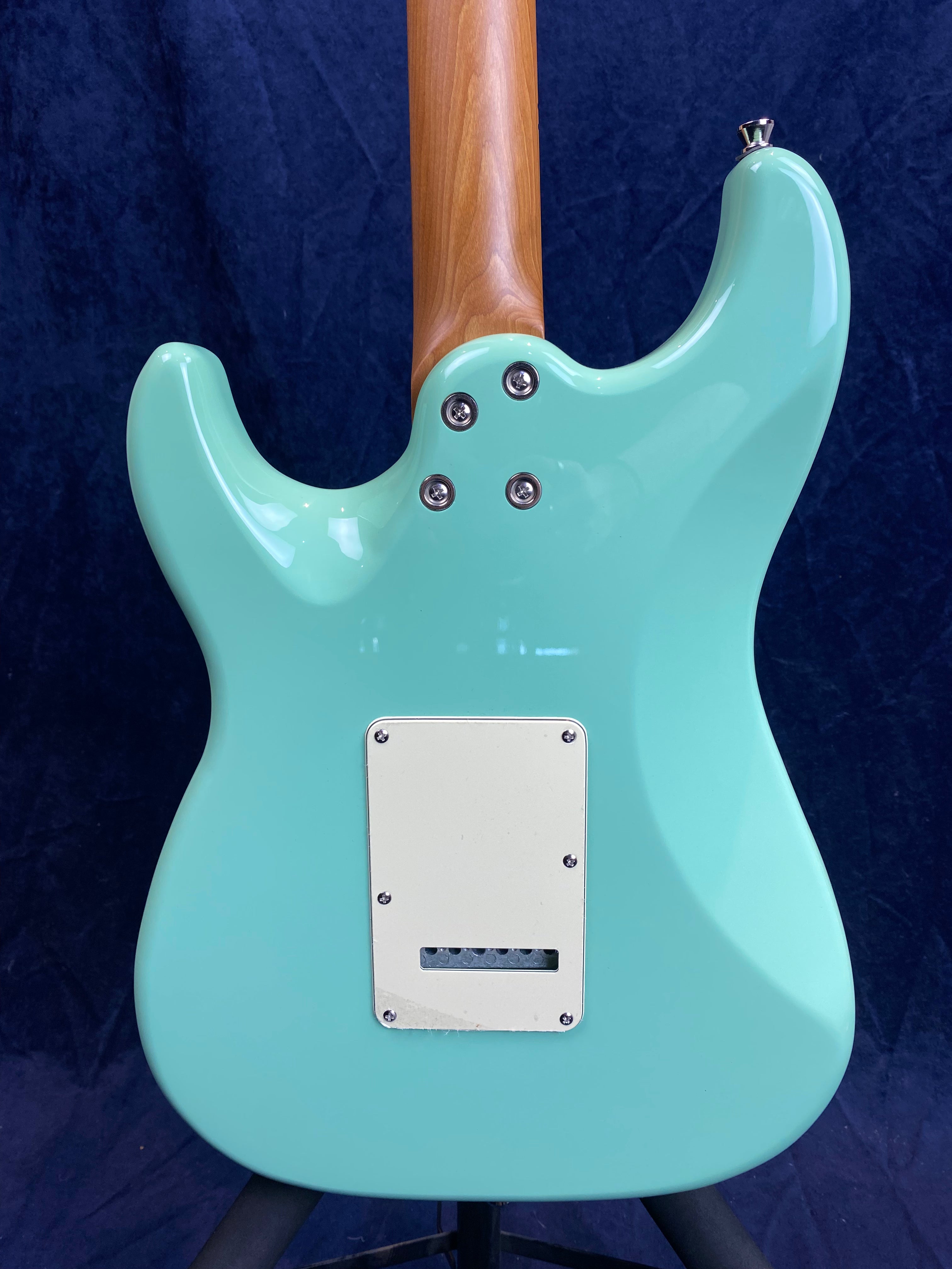 Corps de guitare électrique bleu clair vu de dos, plaque rectangulaire blanche fixée au centre et manche en bois apparent.