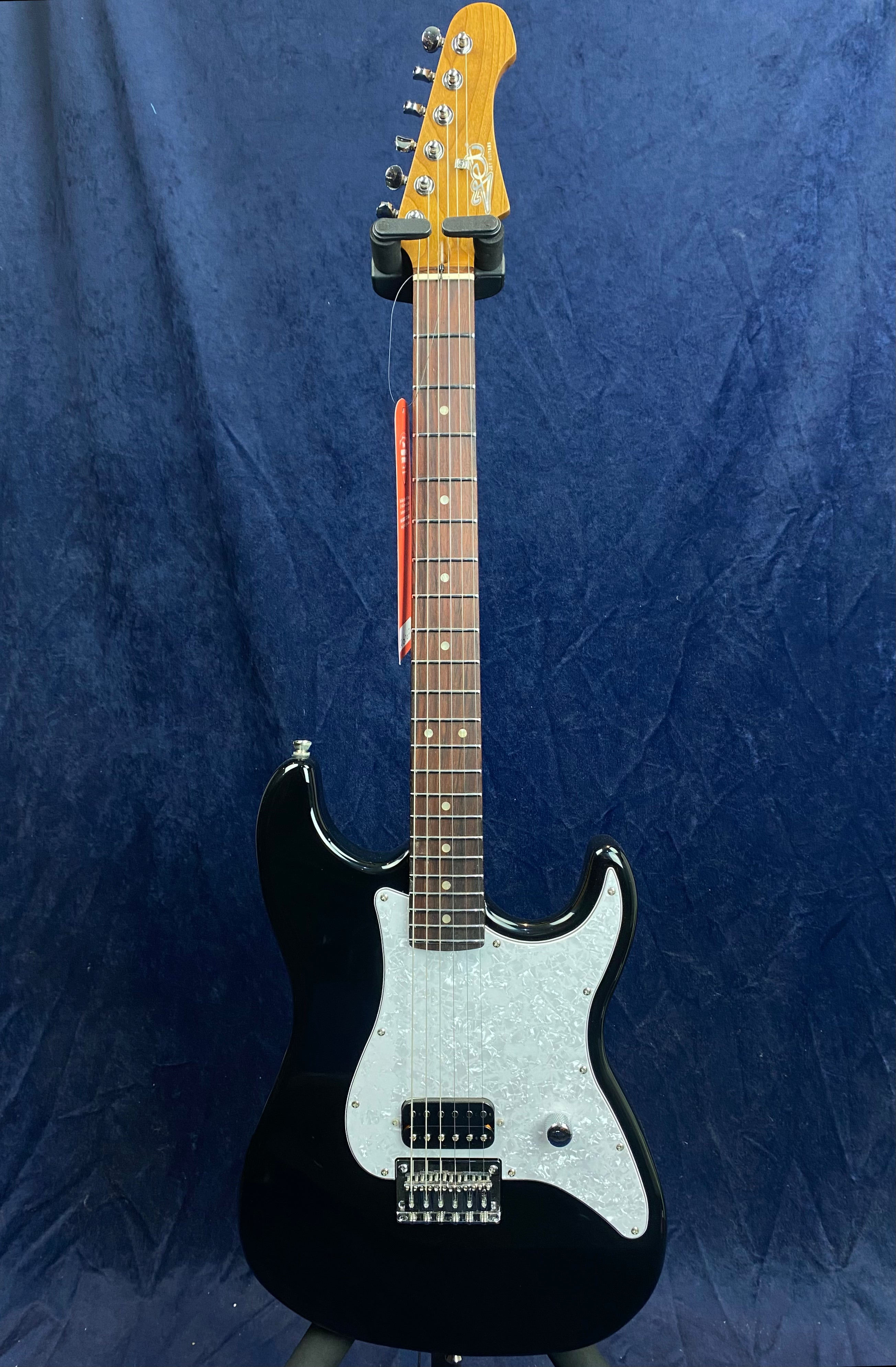 Black electric guitar with a white pearloid pickguard, rosewood fretboard, single humbucker pickup, volume knob, and a six-inline tuner headstock.