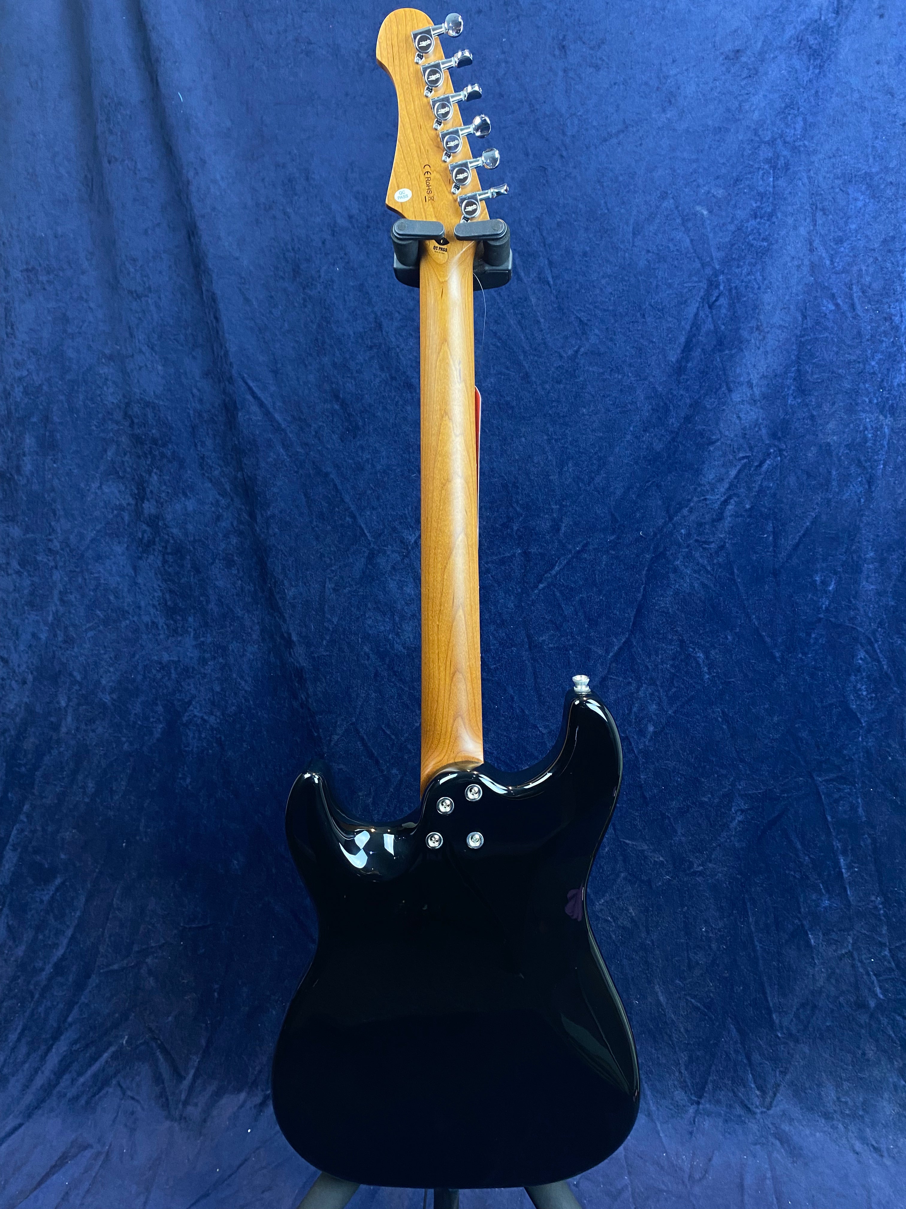 A black electric guitar seen from the back, showing a wooden neck and six tuning pegs against a dark blue background.