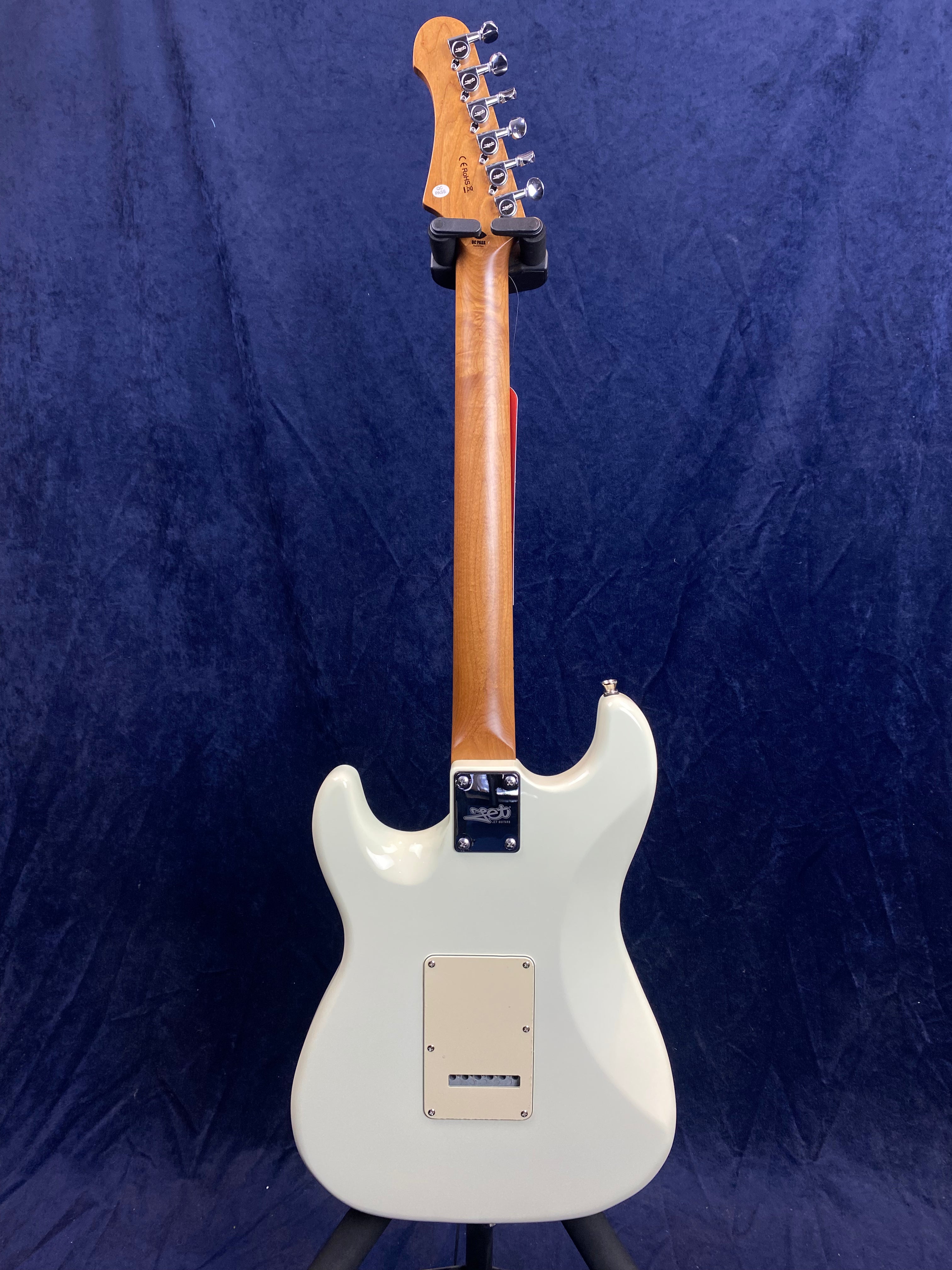 White electric guitar seen from the back, showing a natural wood neck, six tuning pegs, and a rectangular back plate on the body.