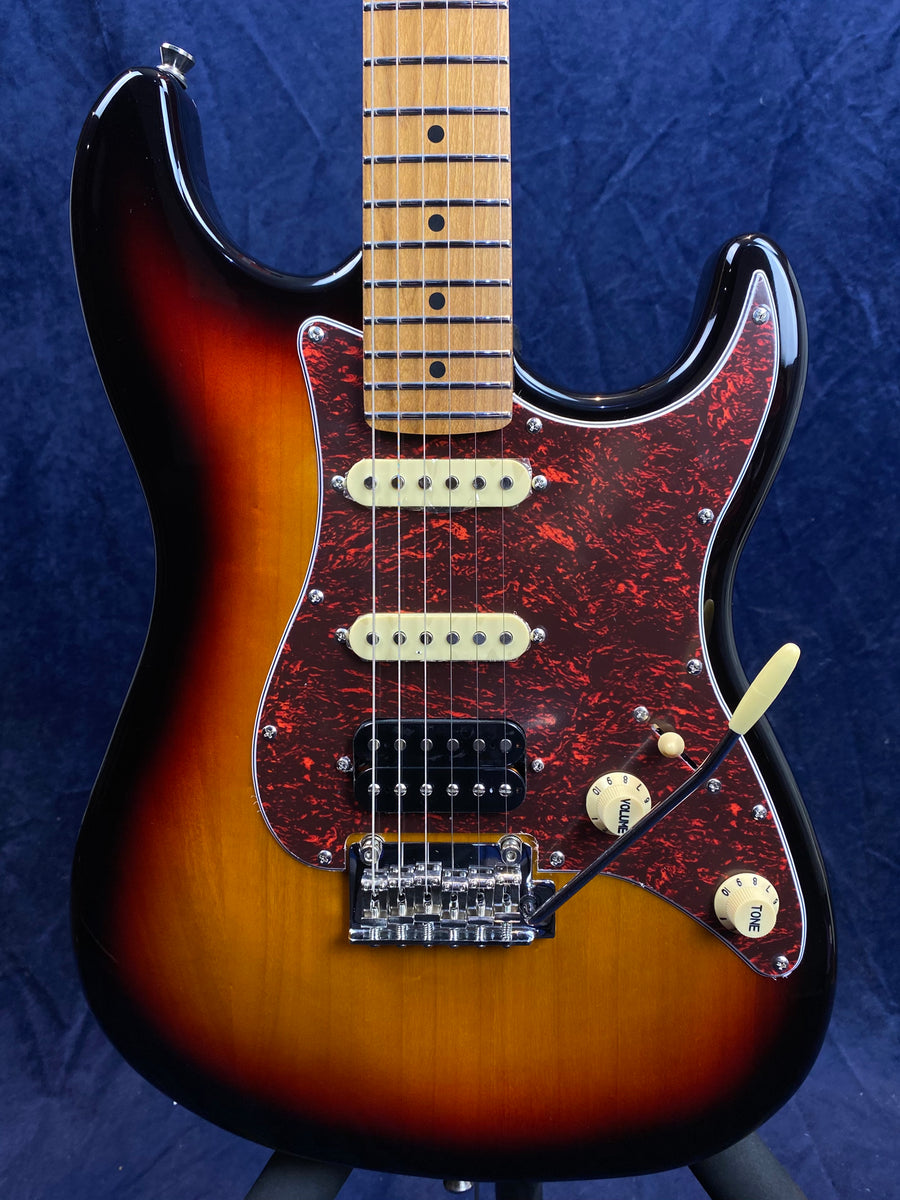 Electric guitar with a sunburst finish, tortoiseshell pickguard, three pickups, and a tremolo arm, set against a dark blue background.