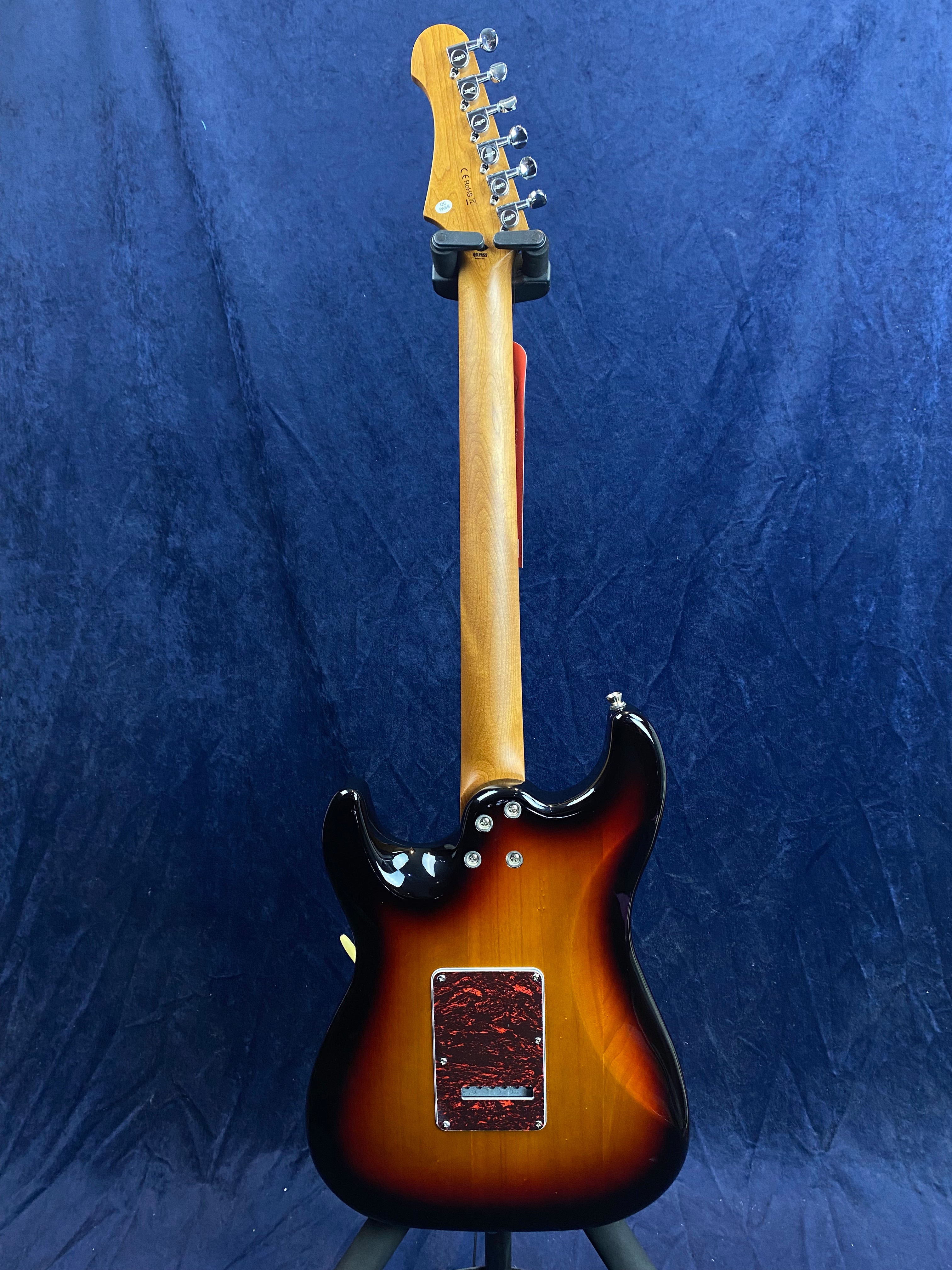 Sunburst electric guitar shown from the back, revealing a maple neck and reddish-brown cover plate on the body, set against a dark blue background.