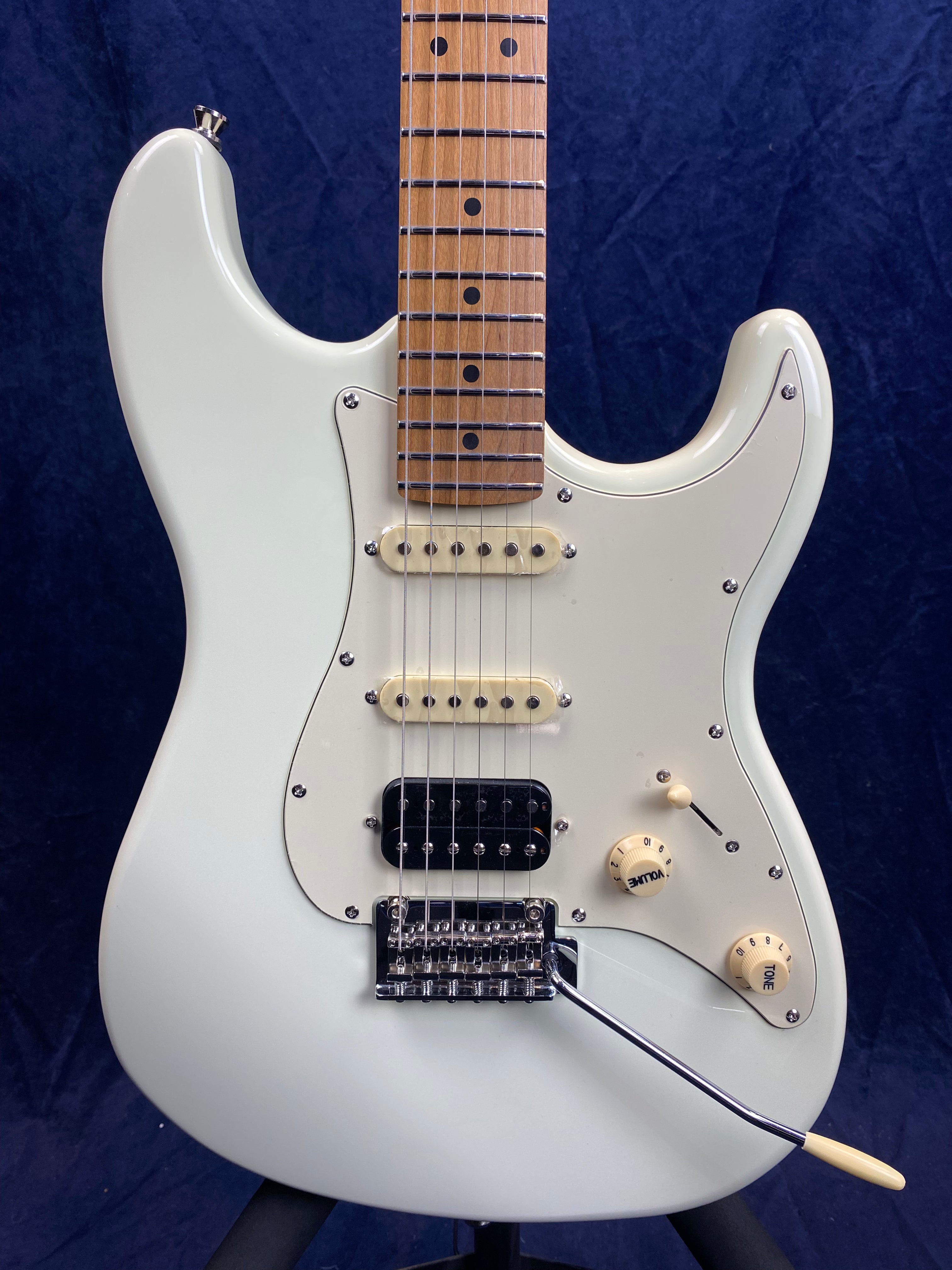White electric guitar with three pickups, two cream knobs labeled volume and tone, chrome tremolo bridge, maple fretboard, and a white pickguard.