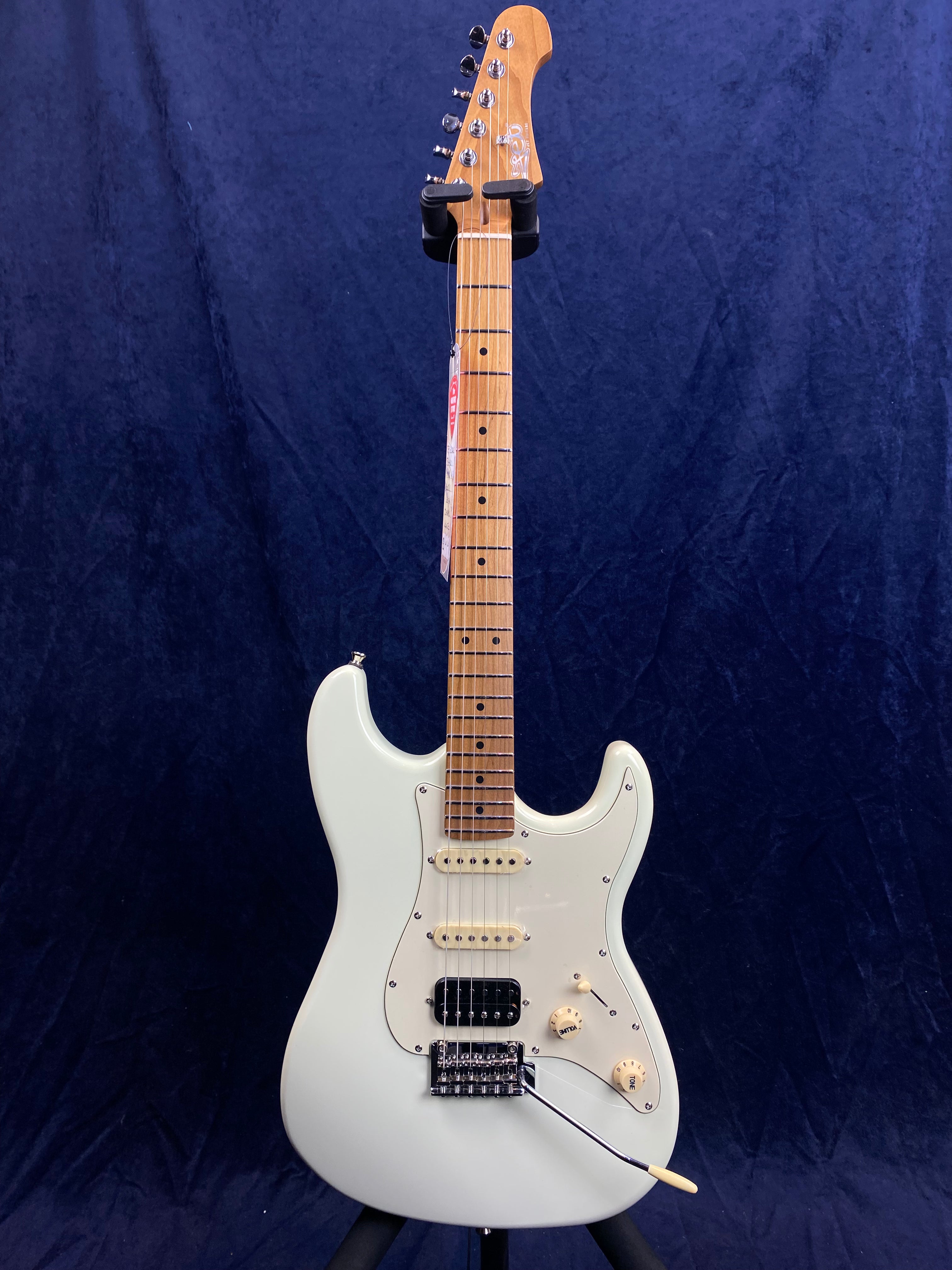 White electric guitar with a maple neck, three pickups, and a whammy bar, set against a dark blue background.