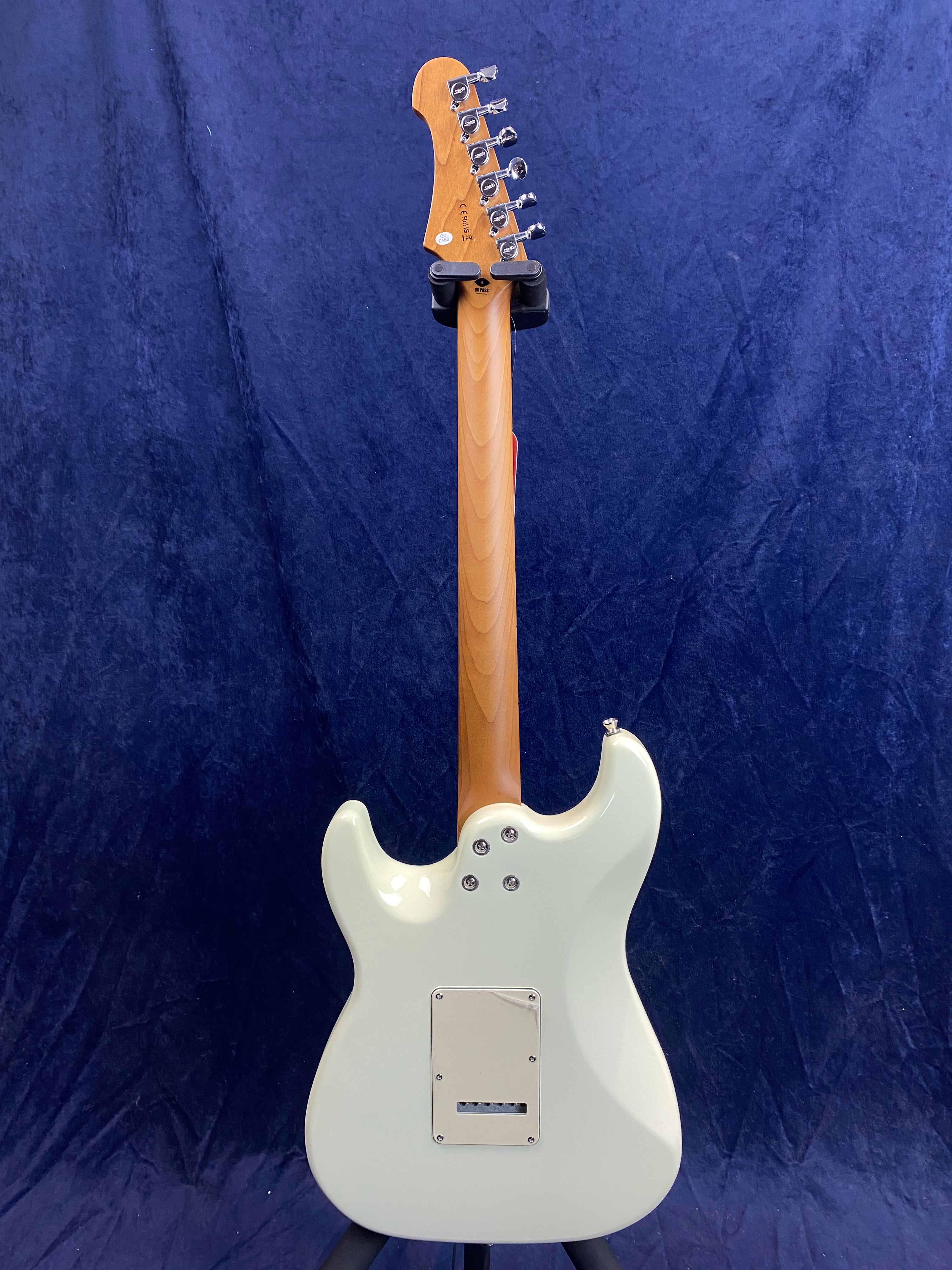 White electric guitar shown from the back, with a natural wood neck and six tuning pegs against a dark blue background.