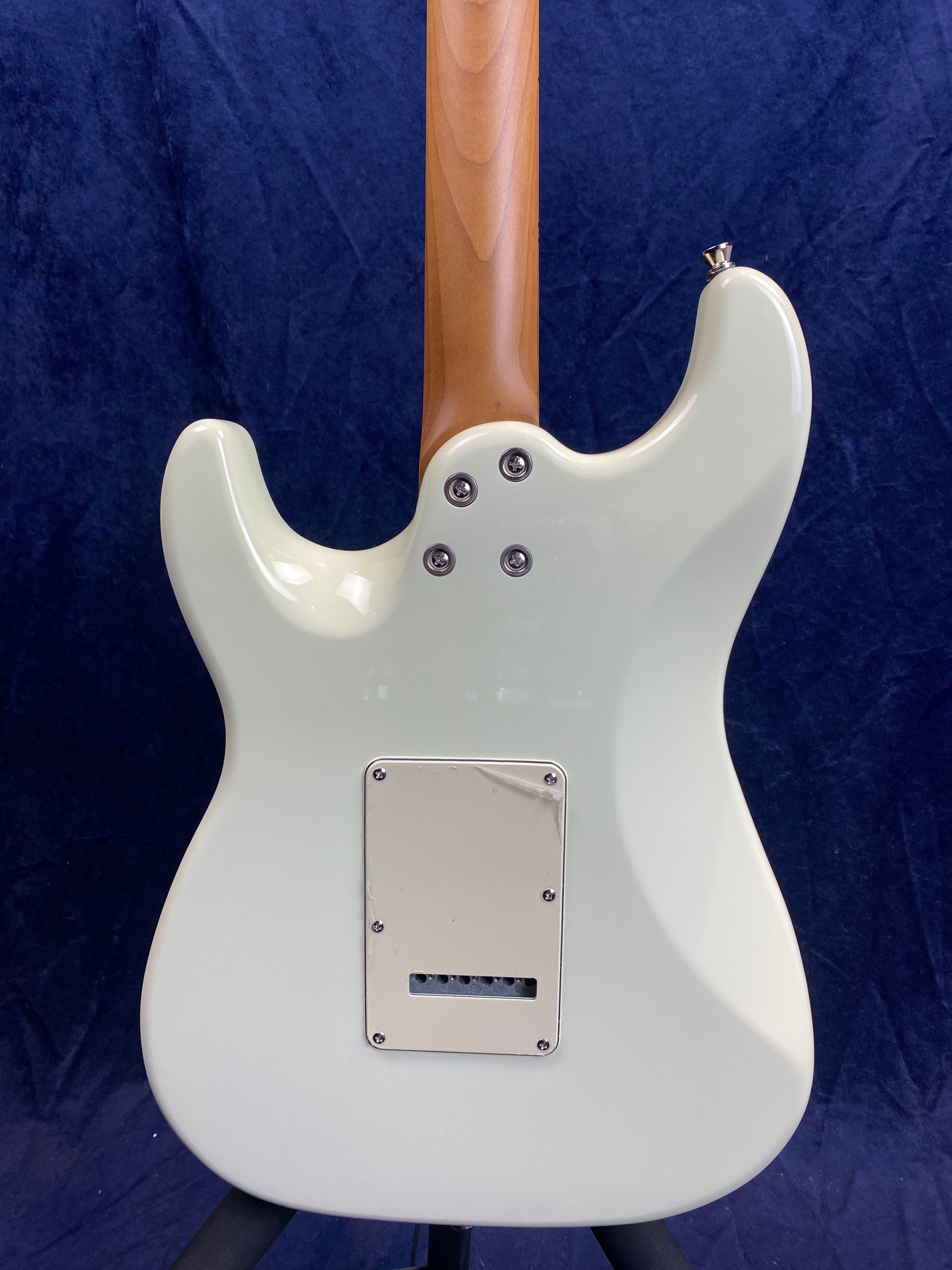 Back of a pale green electric guitar showing a natural wood neck, four neck screws, and a rectangular back plate with six holes.