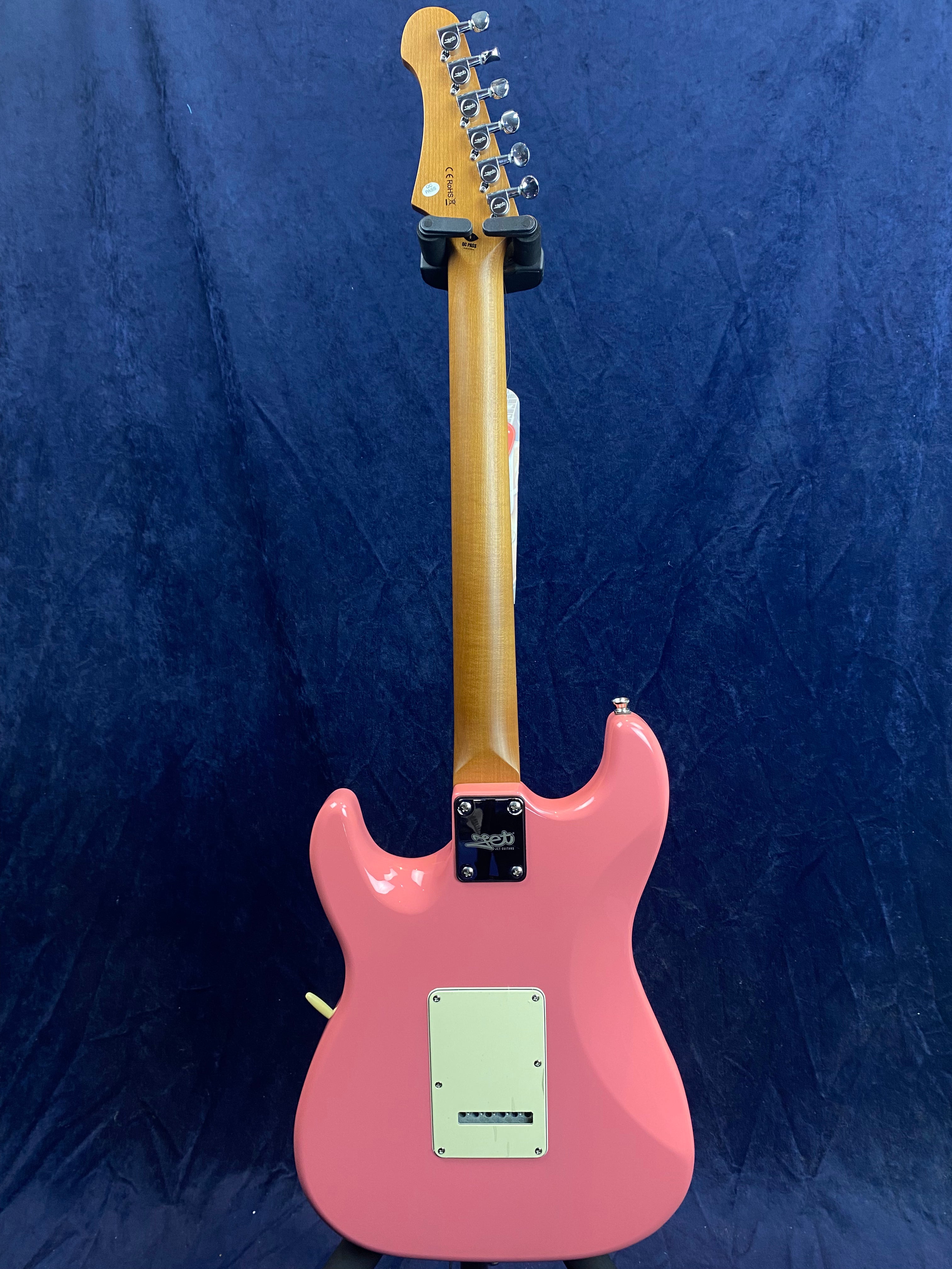 Electric guitar with a glossy pink body, light wood neck, and chrome tuning pegs, shown from the back against a dark blue background.