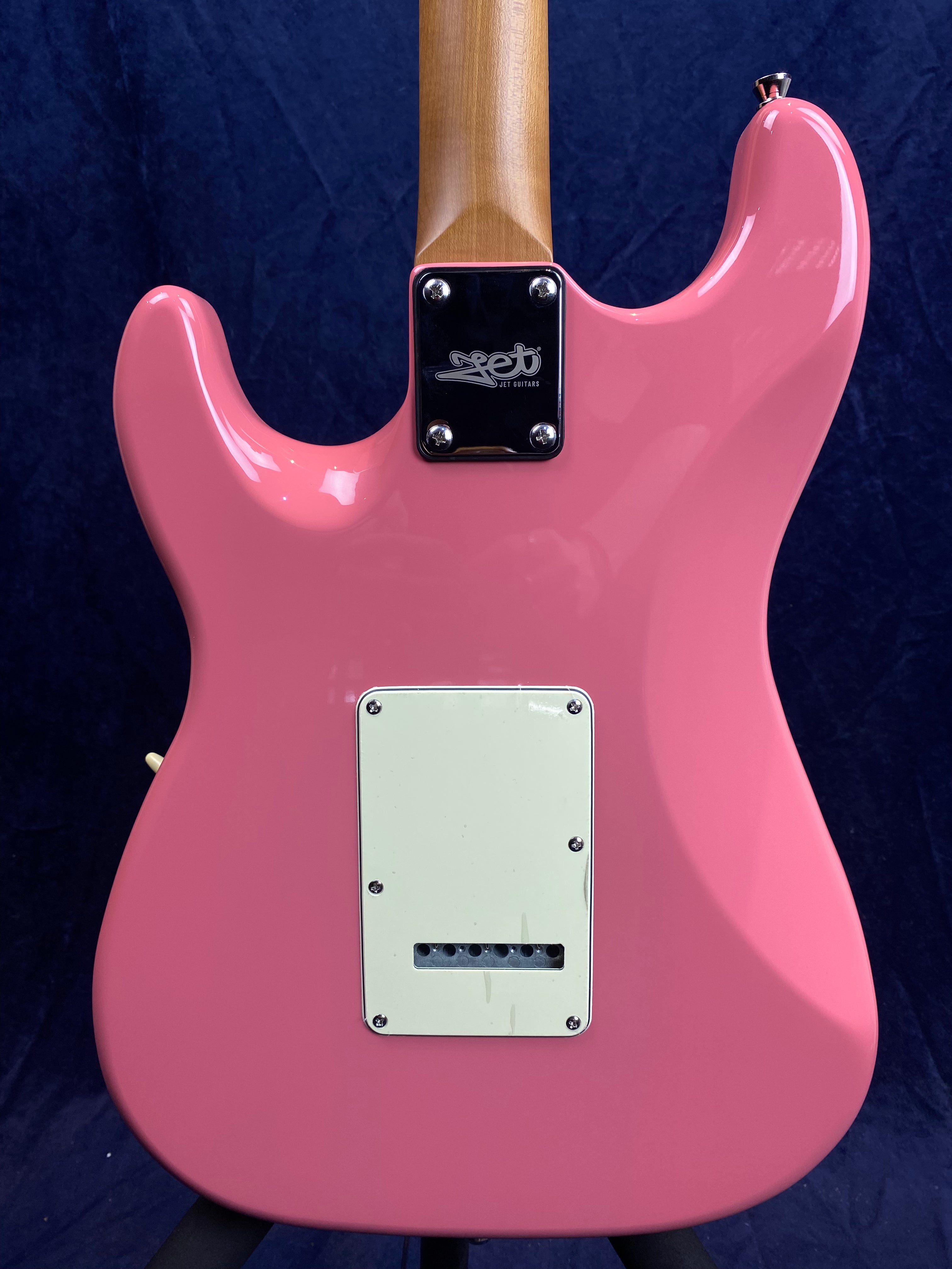 The back of a pink electric guitar with a white rectangular cover plate and a bolt-on neck joint, set against a dark background.