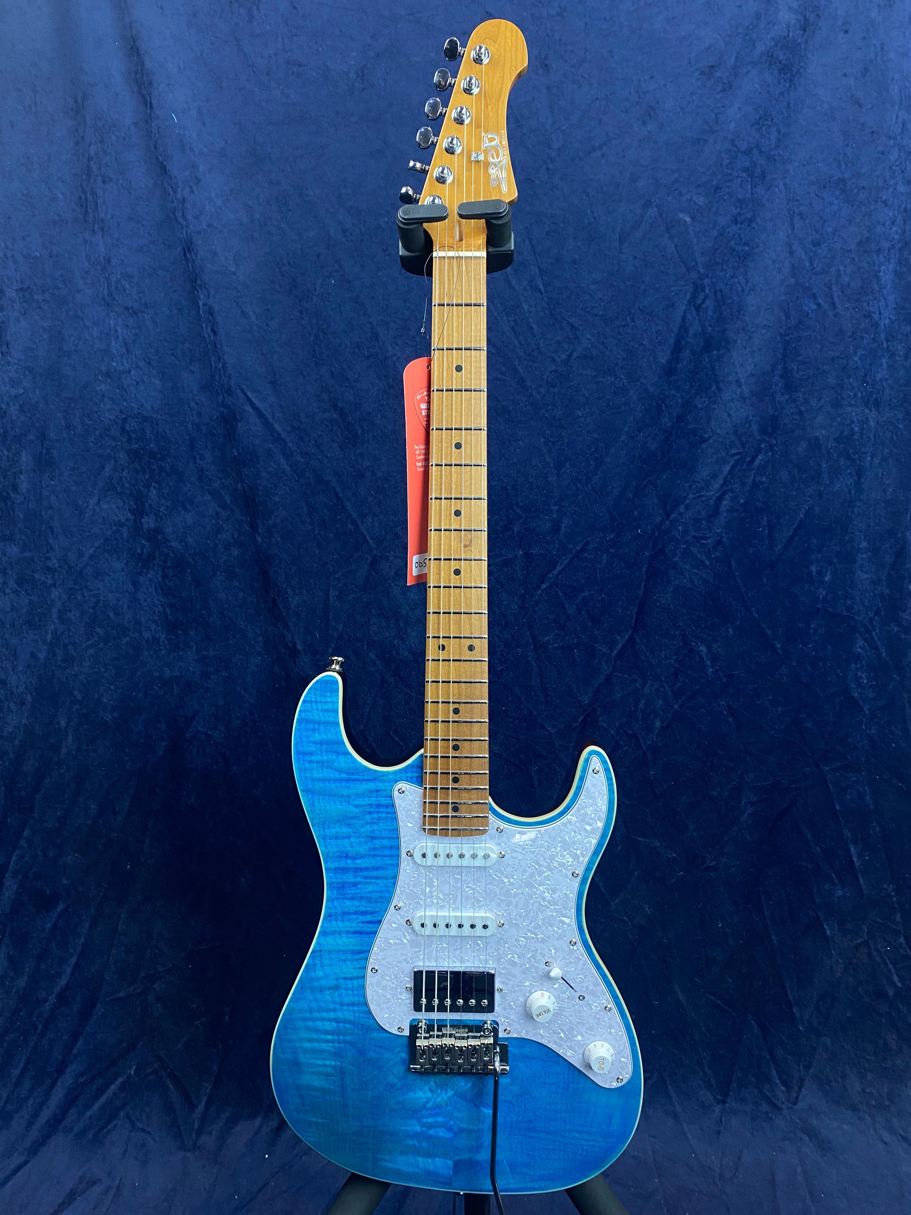 Electric guitar with a bright blue body, white pickguard, maple neck, and three pickups, displayed upright against a dark blue background.