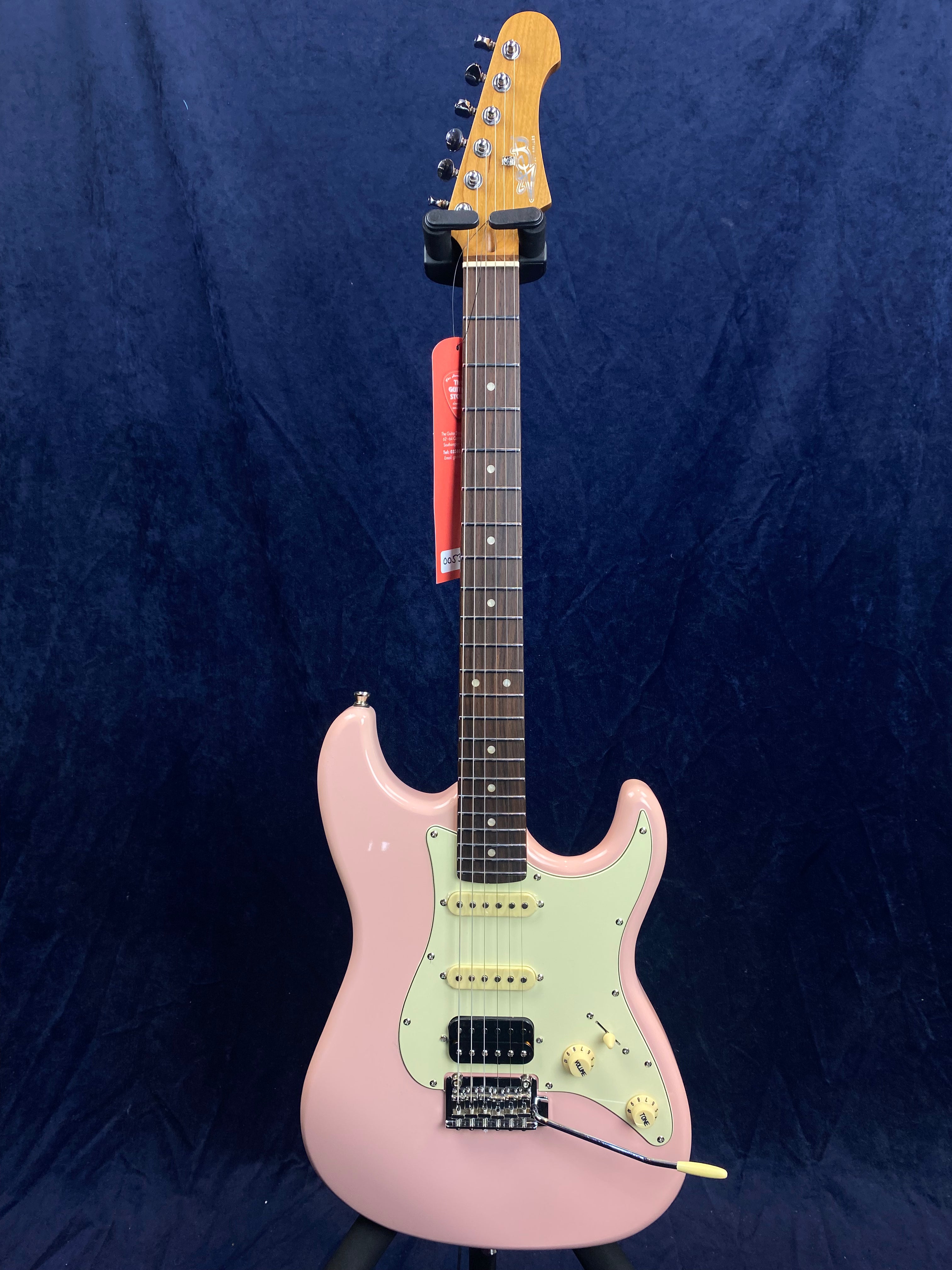 Electric guitar with a light pink body, white pickguard, three pickups, and a tremolo arm. The neck is brown wood with silver frets and dot inlays.