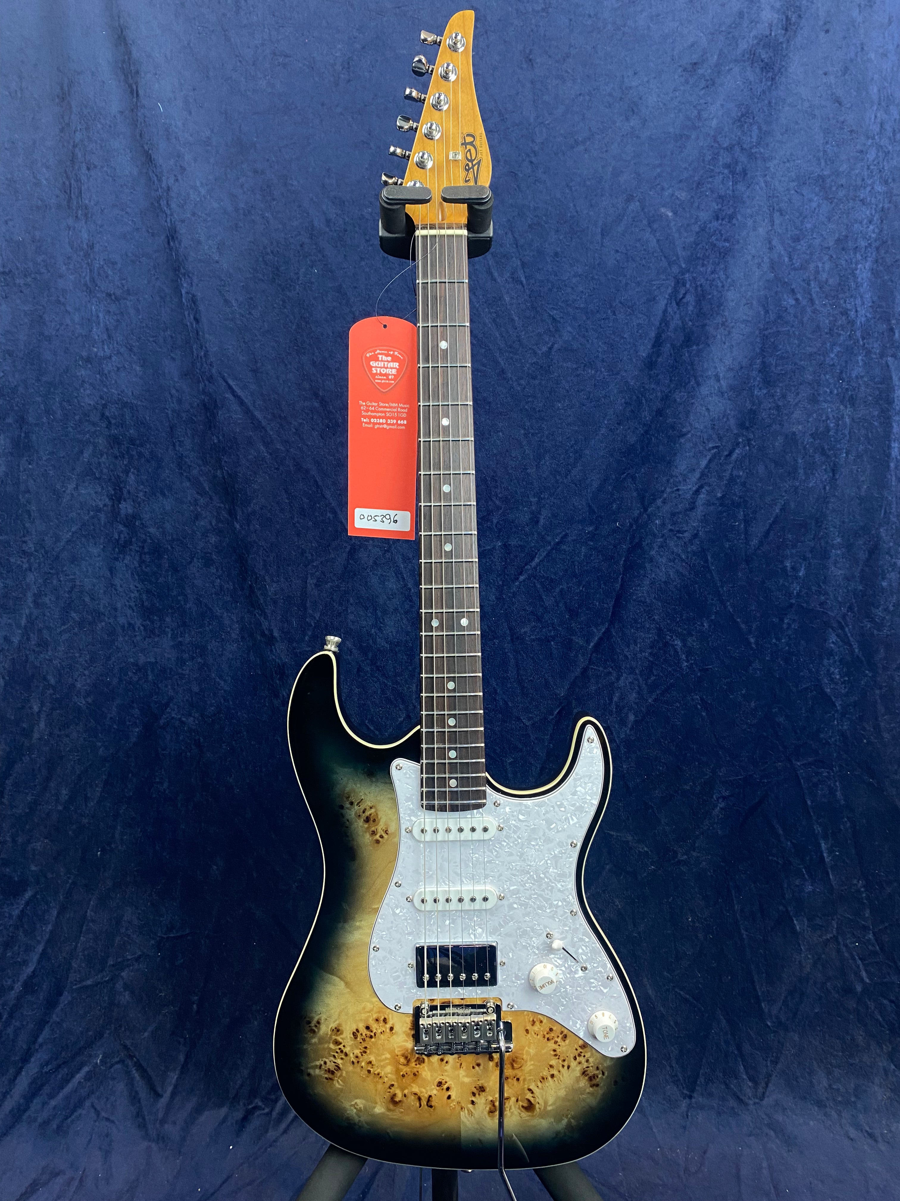 Sunburst-finish electric guitar with a white pearloid pickguard, three pickups, six tuning pegs, and a red tag hanging from the headstock.
